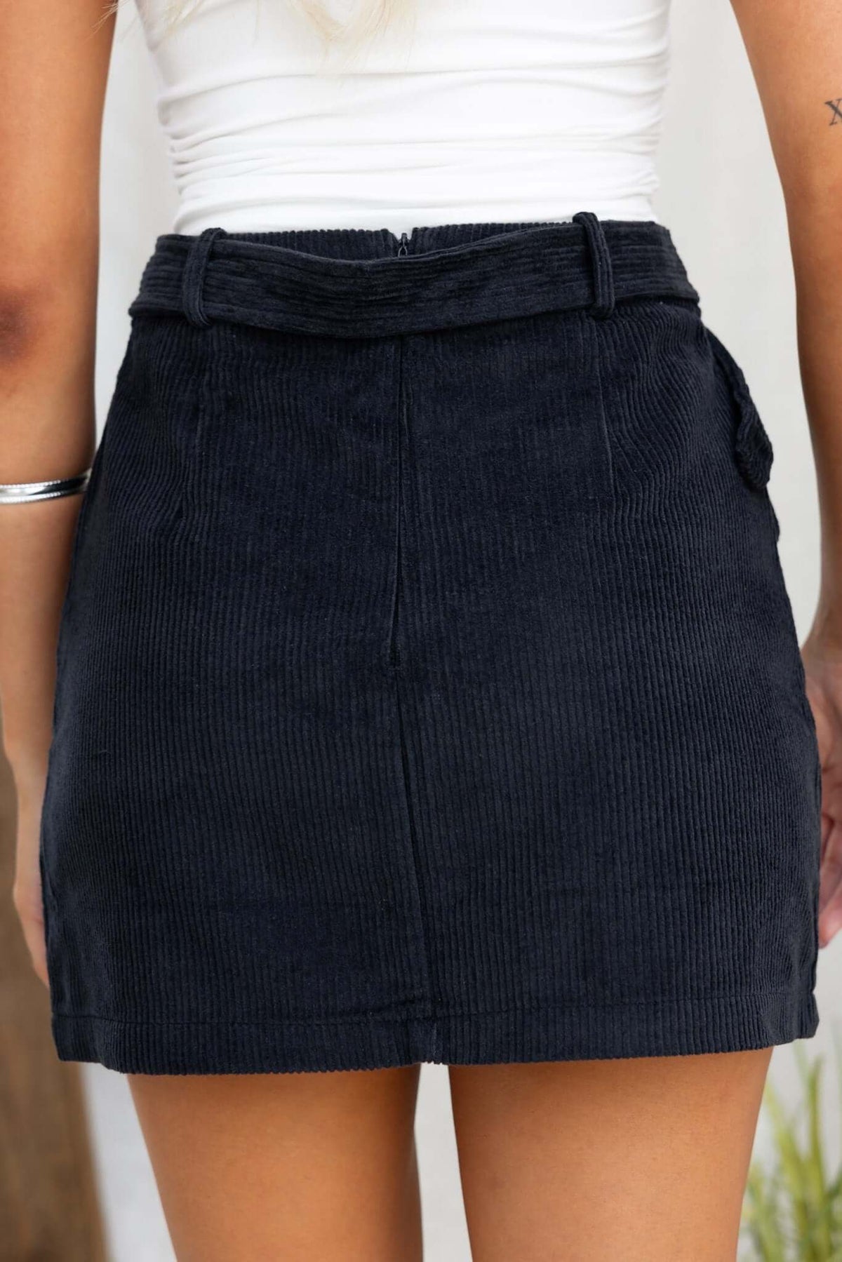 Back view of a black corduroy Pierre Skirt featuring a mid-high waist, removable belt, and pockets.