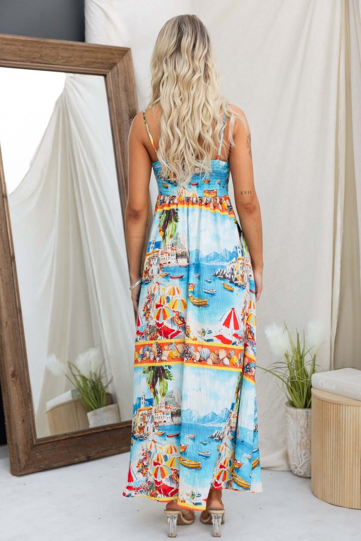Model wearing Salilah Maxi Dress with vibrant beach print, showcasing adjustable straps and shirred back, view from the back.