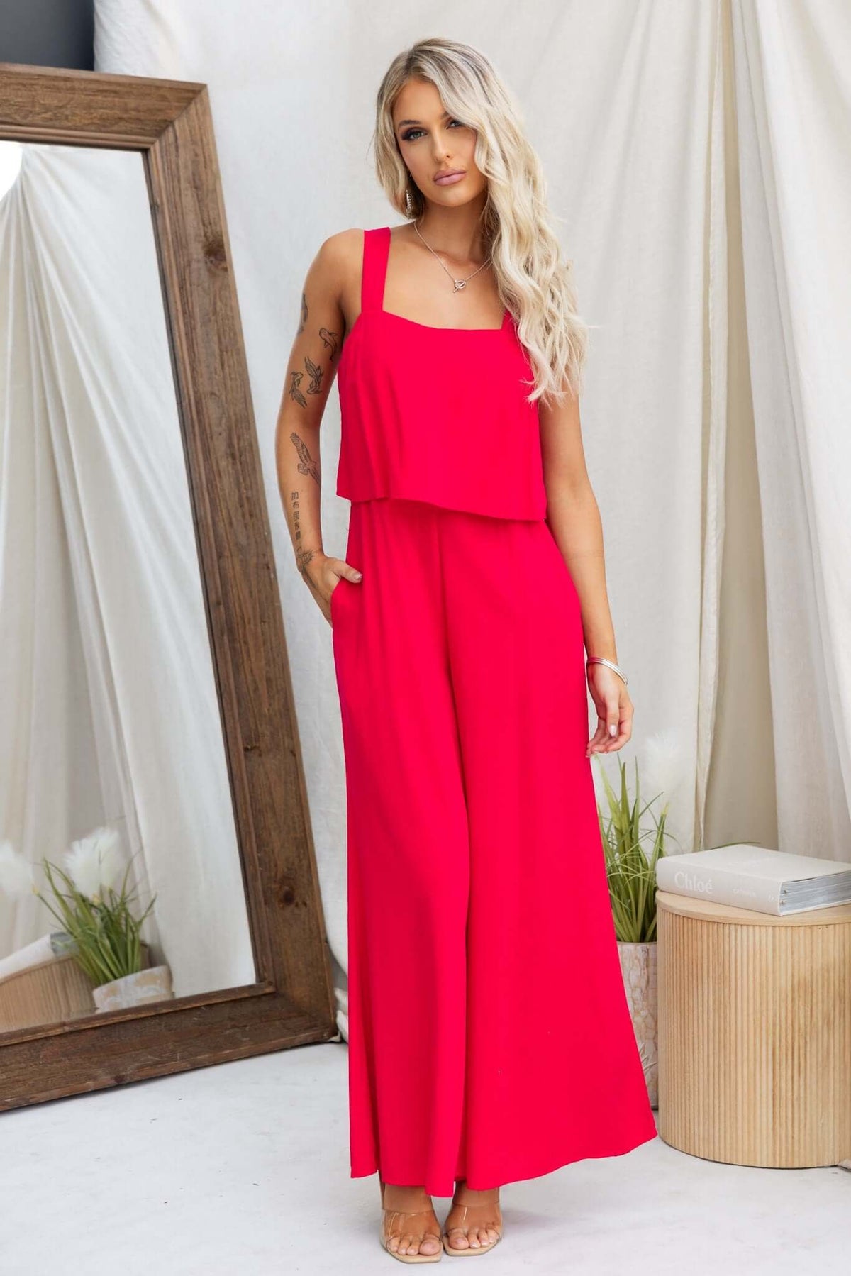 Bright pink Verko jumpsuit with pockets and an elastic back, styled with sandals in a chic setting.