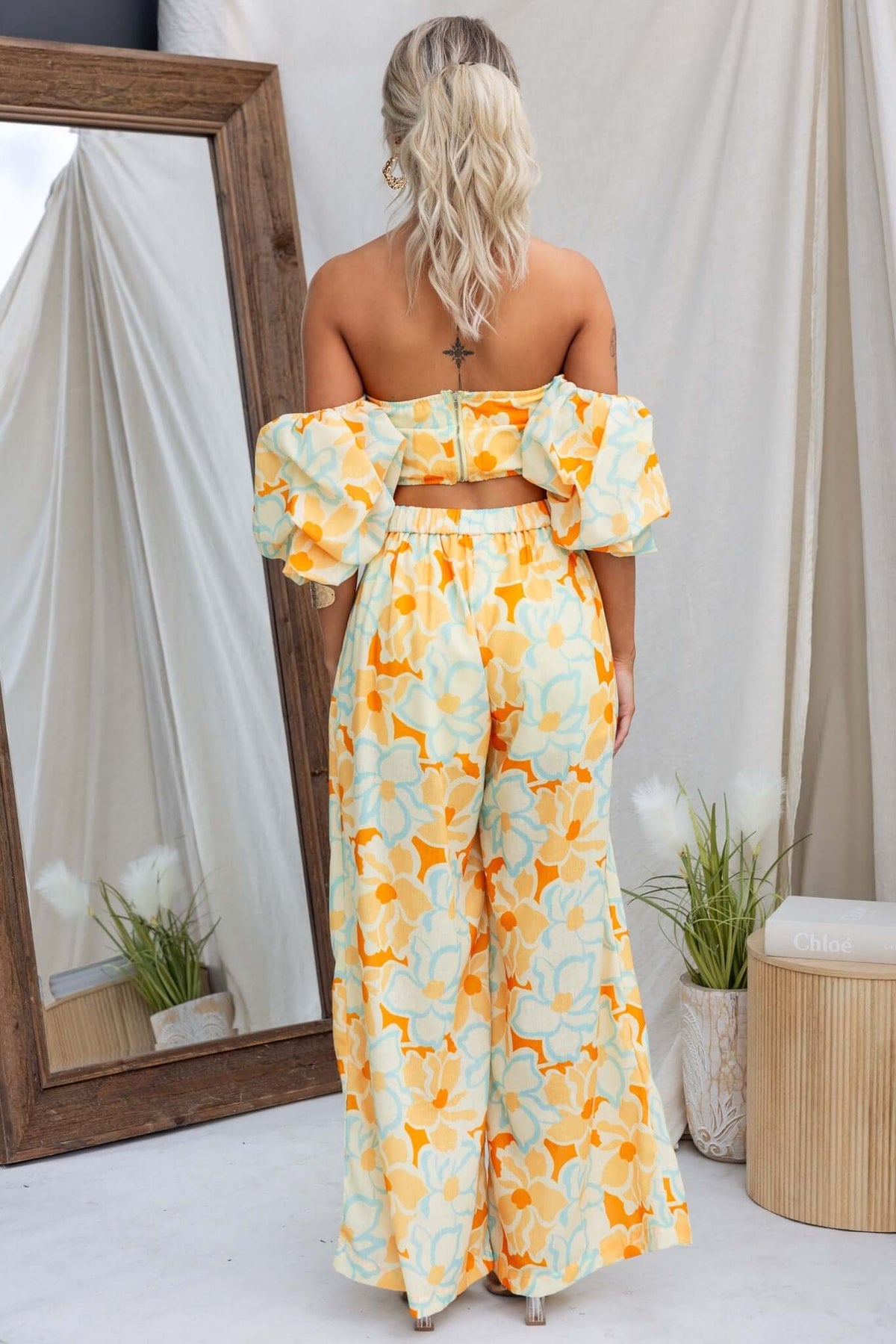 Woman wearing Olessia Set, featuring a floral crop top and wide-leg pants in pastel colors, showcasing the back view.