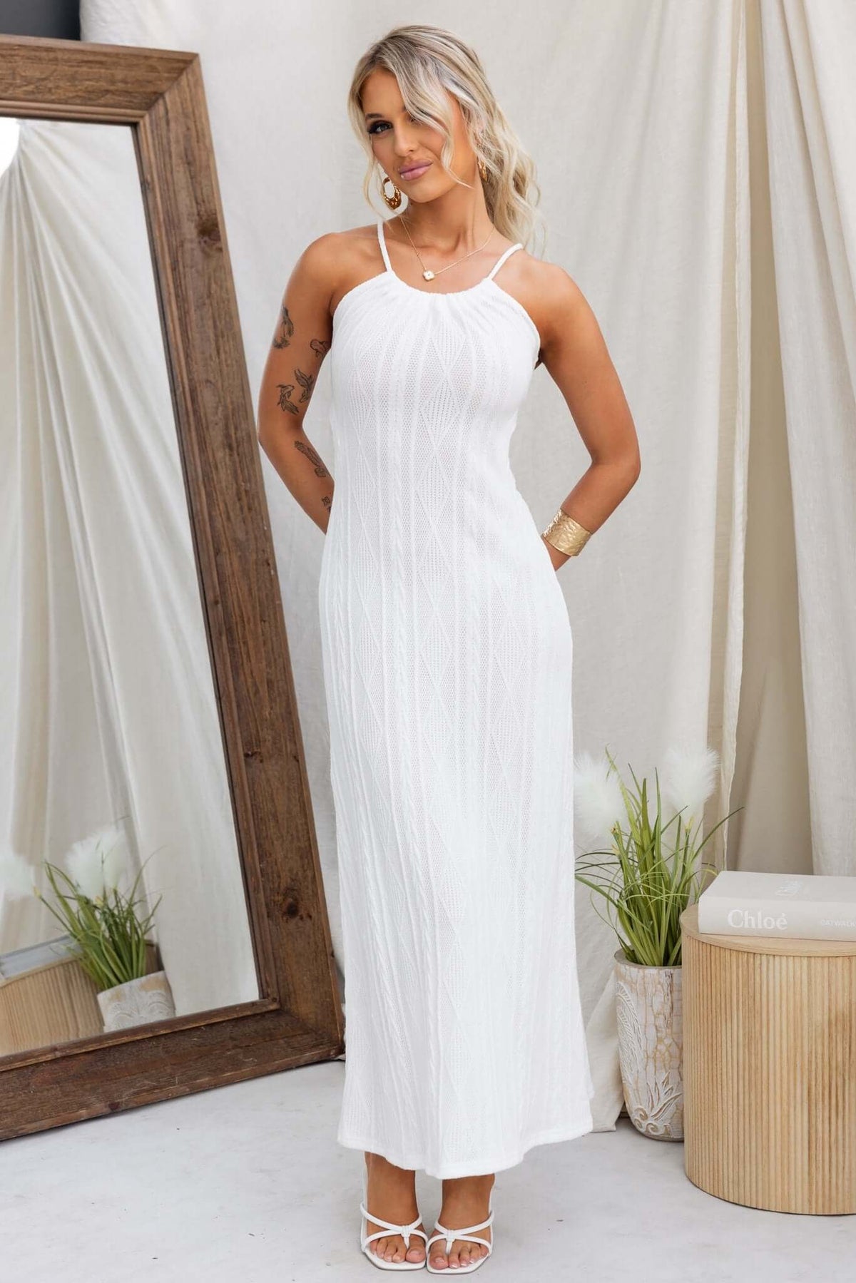 Model wearing Dream Weaver Maxi Dress, a stylish white knit gown with a tie neckline and cut-out back.