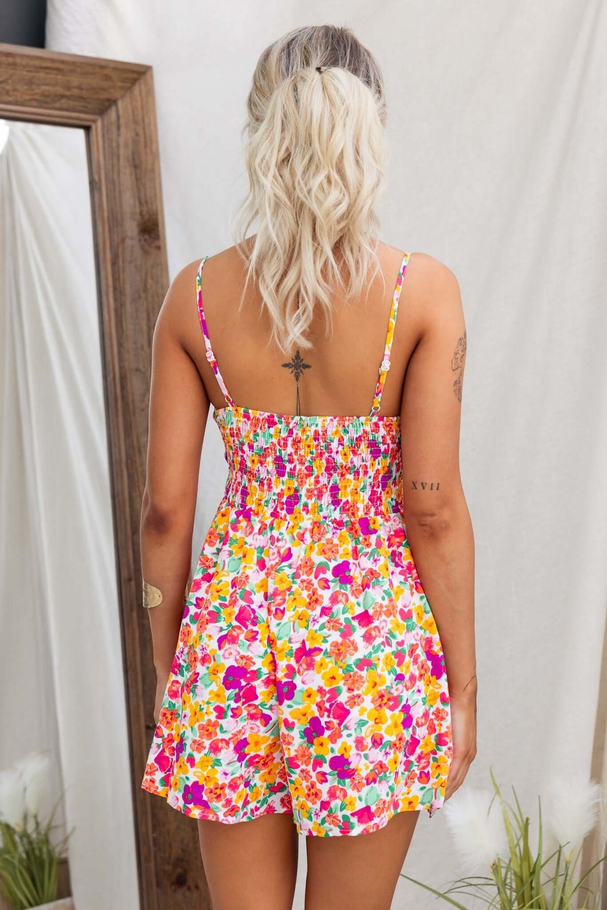 Back view of a woman in a colorful floral Kaycee Playsuit with adjustable straps and smocked bodice.