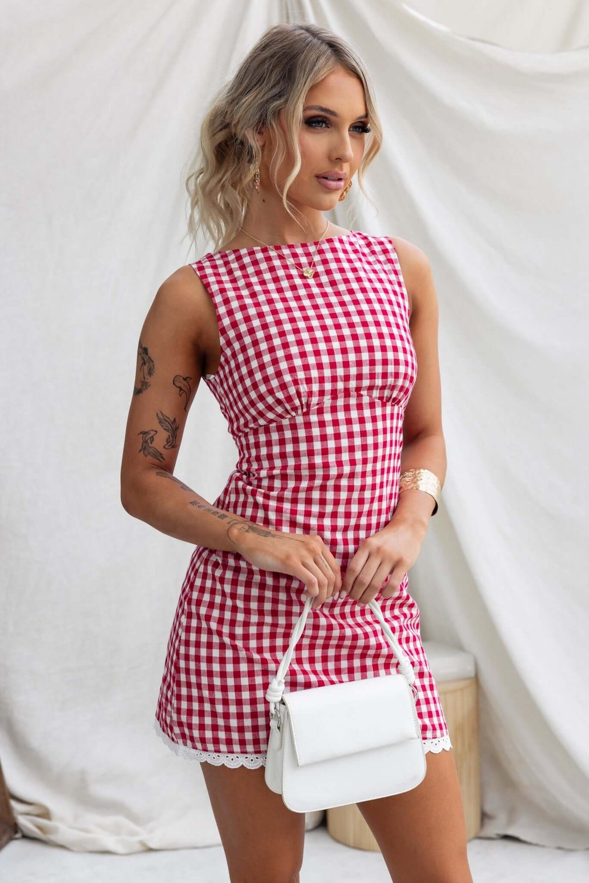 Model wearing Kairyn Dress, a red and white gingham dress with a high neckline and sleeveless design.