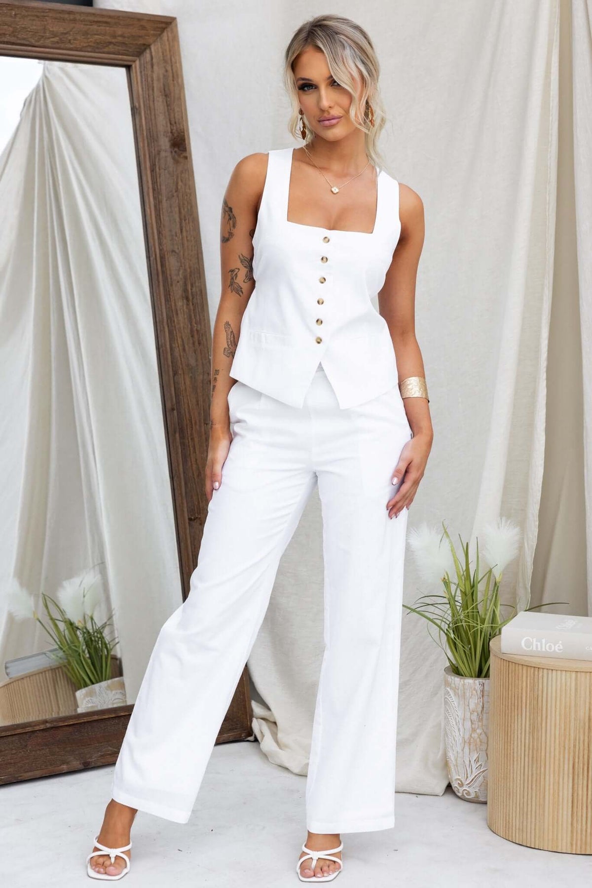 Model wearing a white Vaylor Top with square neckline, button-up front, and wide-legged pants, styled with jewelry.