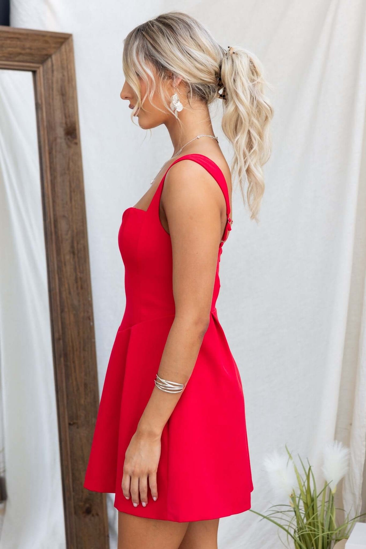 Side view of a woman wearing a red Franklin Dress with adjustable straps and a fitted bust.