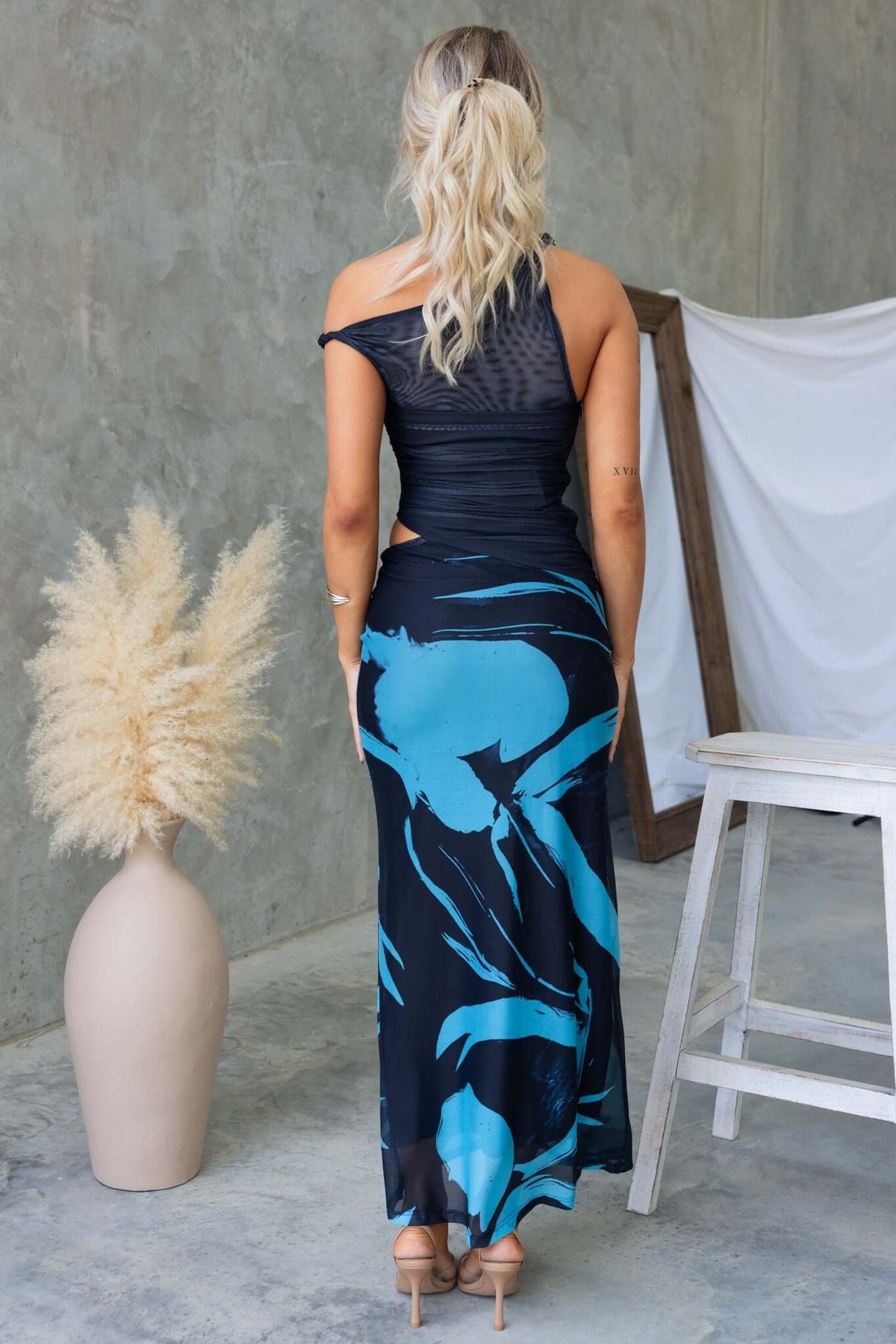 Back view of a woman wearing the Ovolo Maxi Dress featuring a cut-out side, mesh fabric, and rolled shoulder detail.