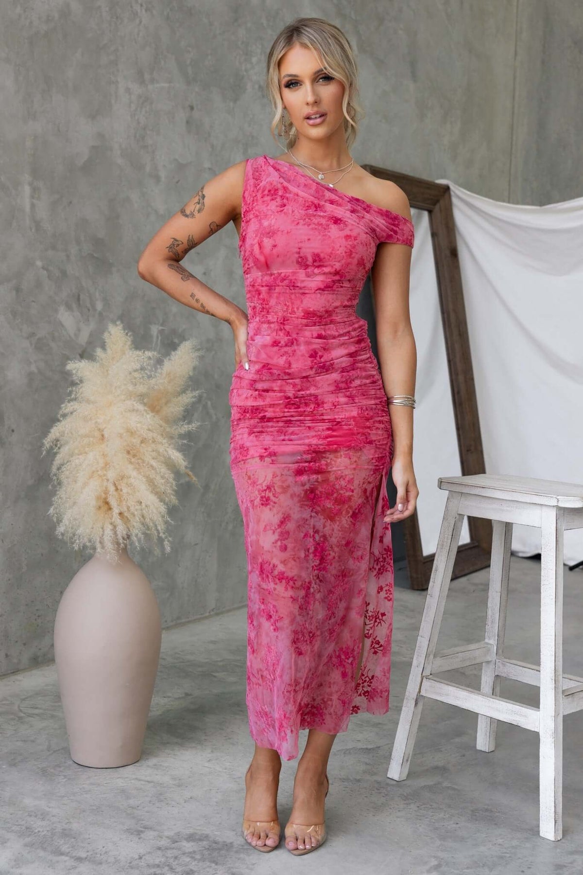Model wearing a pink asymmetric Marino Maxi Dress featuring a side split and mesh material, styled with a chic backdrop.