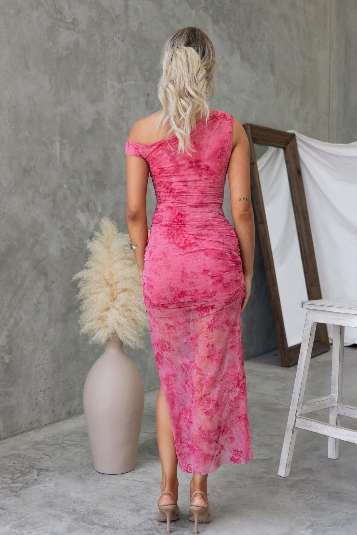 Back view of a model in a pink Marino maxi dress with an asymmetric neckline and side split.