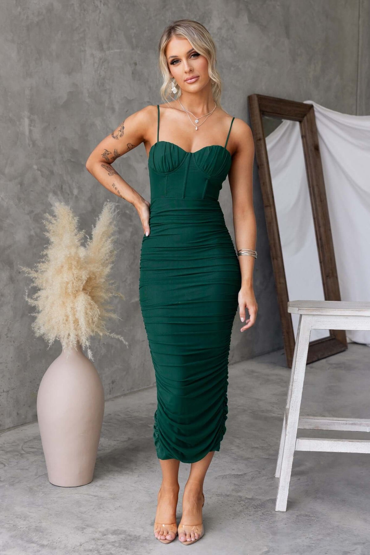 Overboard Midi Dress in green with padded bust, adjustable straps, and ruched detailing, styled in a modern interior.
