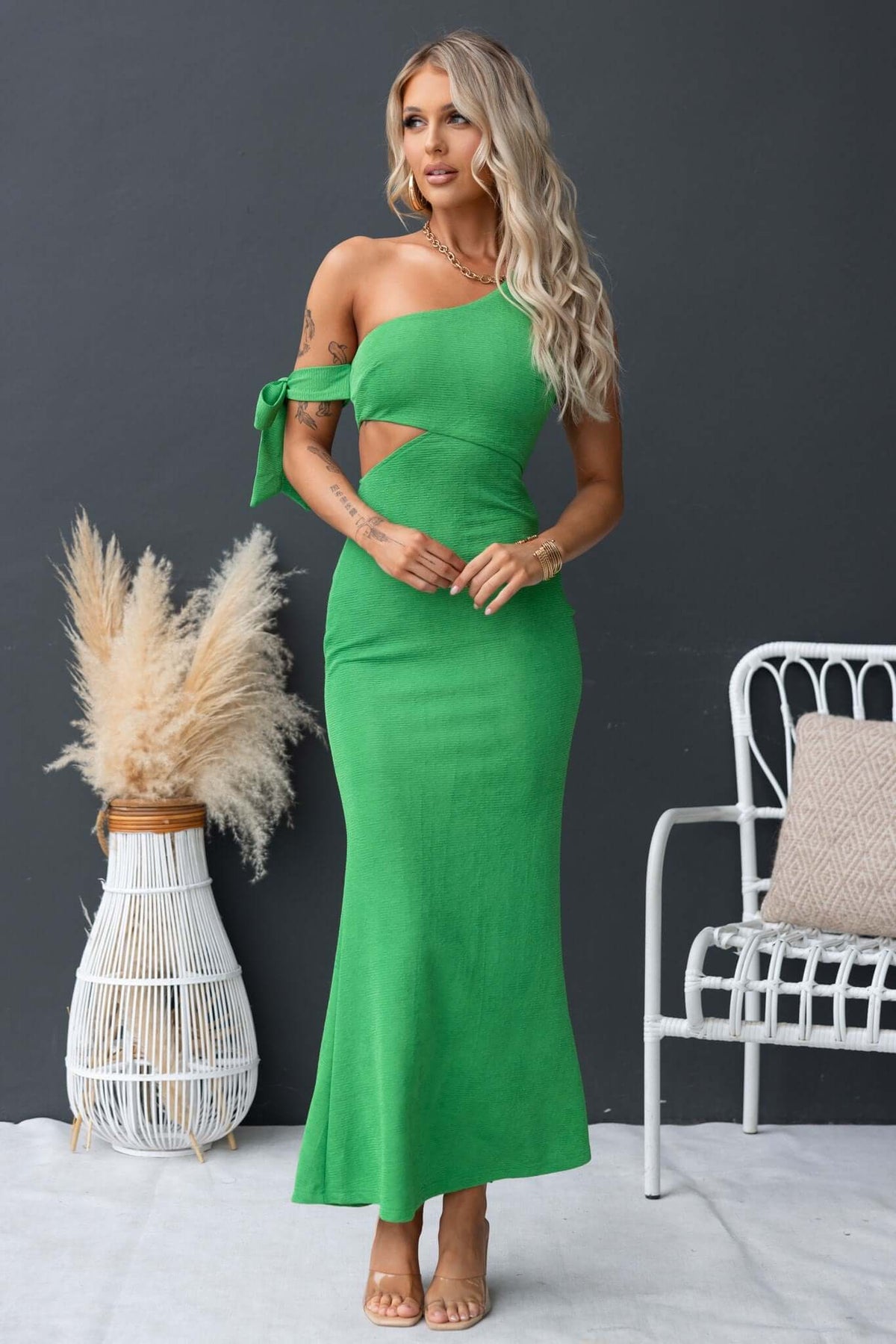 Model wearing a green Malian maxi dress with a one-shoulder neckline and cut-out details, styled with accessories.