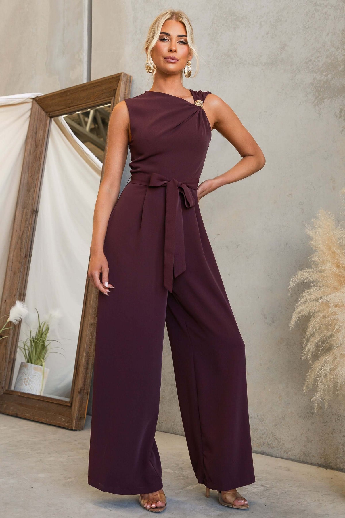 Model wearing an Applause Jumpsuit in burgundy with gold hardware and tie detail.