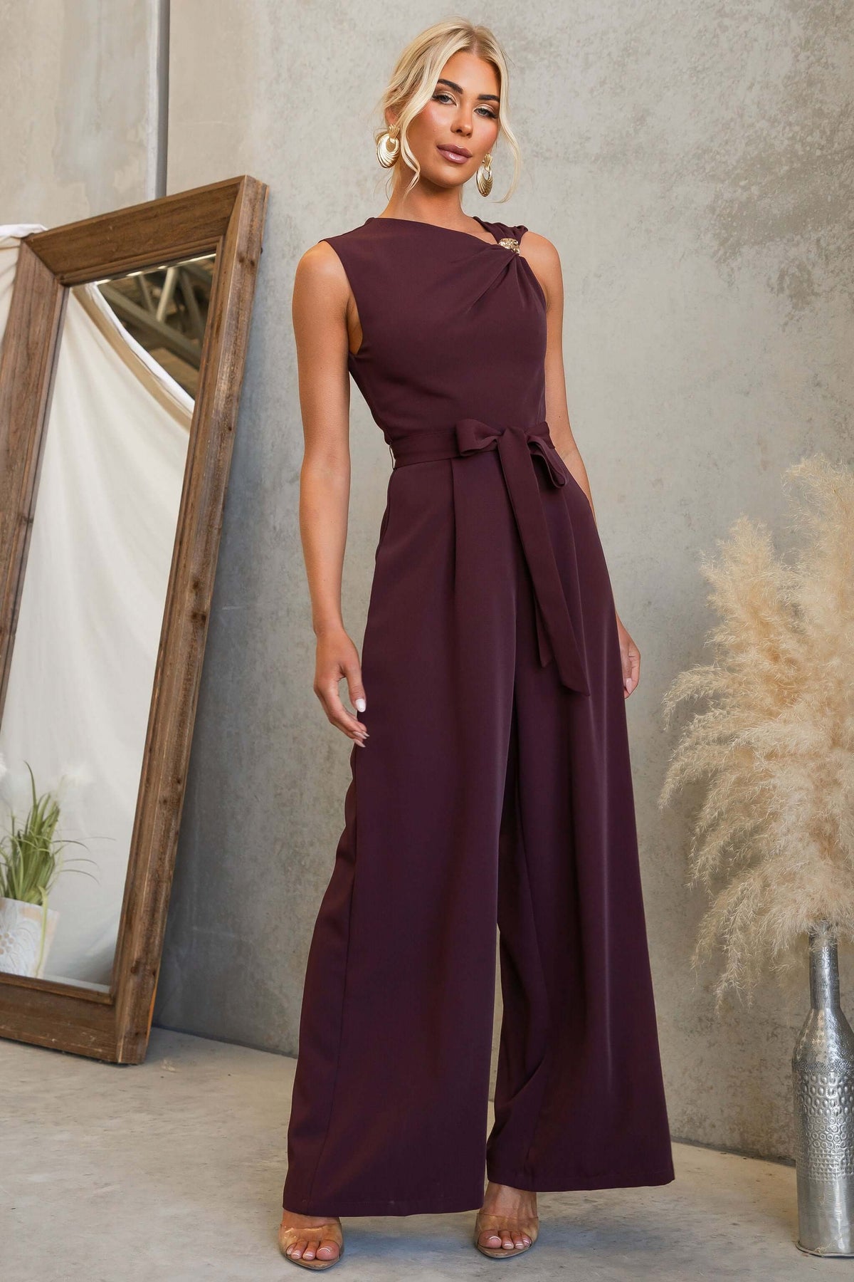 Model showcasing the Applause Jumpsuit with asymmetric neckline and gold hardware.