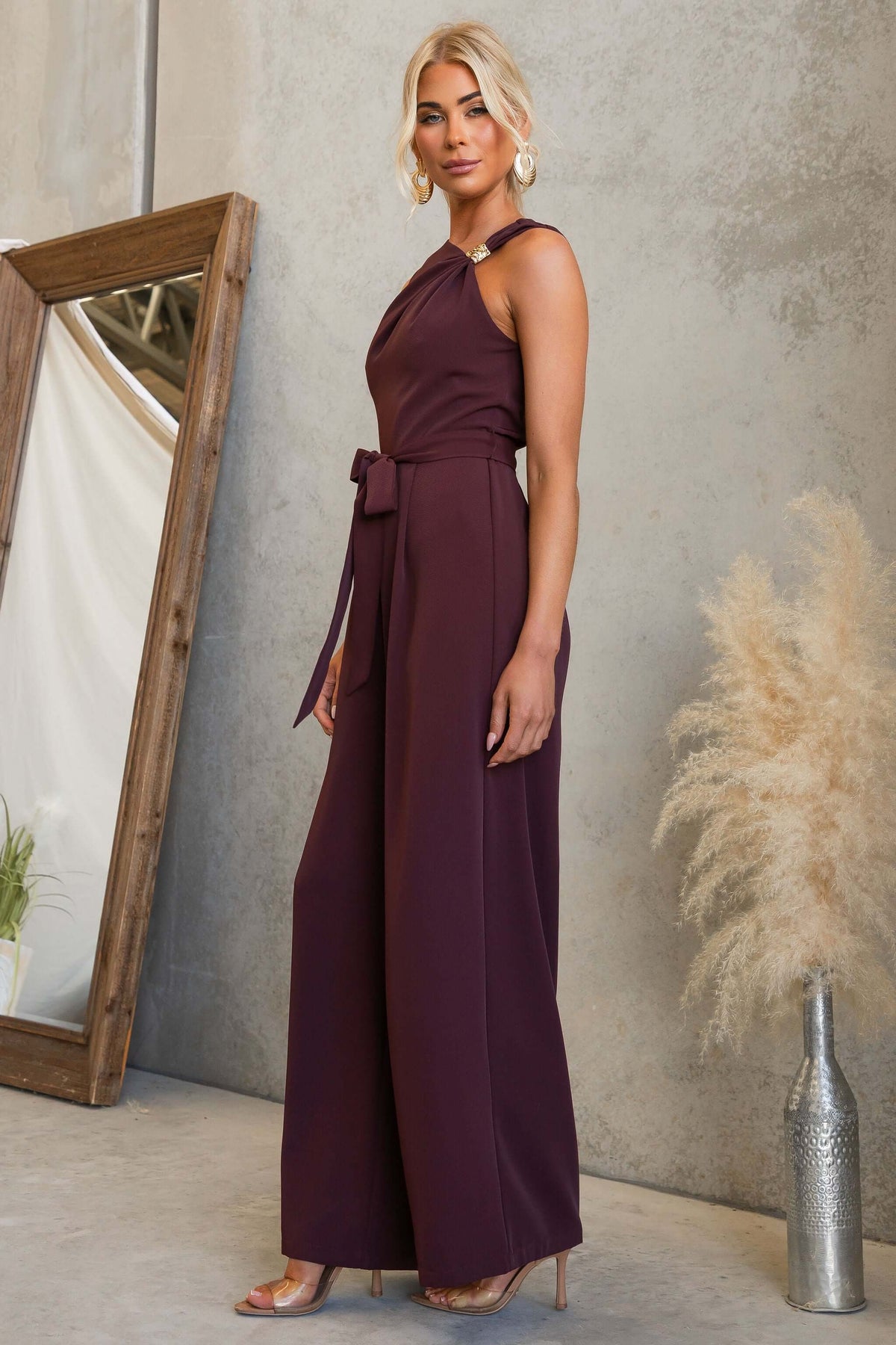 Model wearing Applause Jumpsuit featuring asymmetric neckline and gold hardware, styled with removable tie.