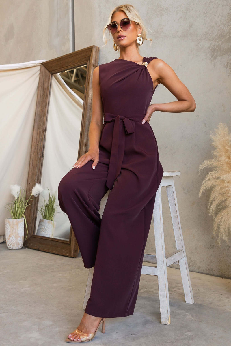 Model wearing Applause Jumpsuit featuring asymmetric neckline and removable tie, styled with sunglasses.