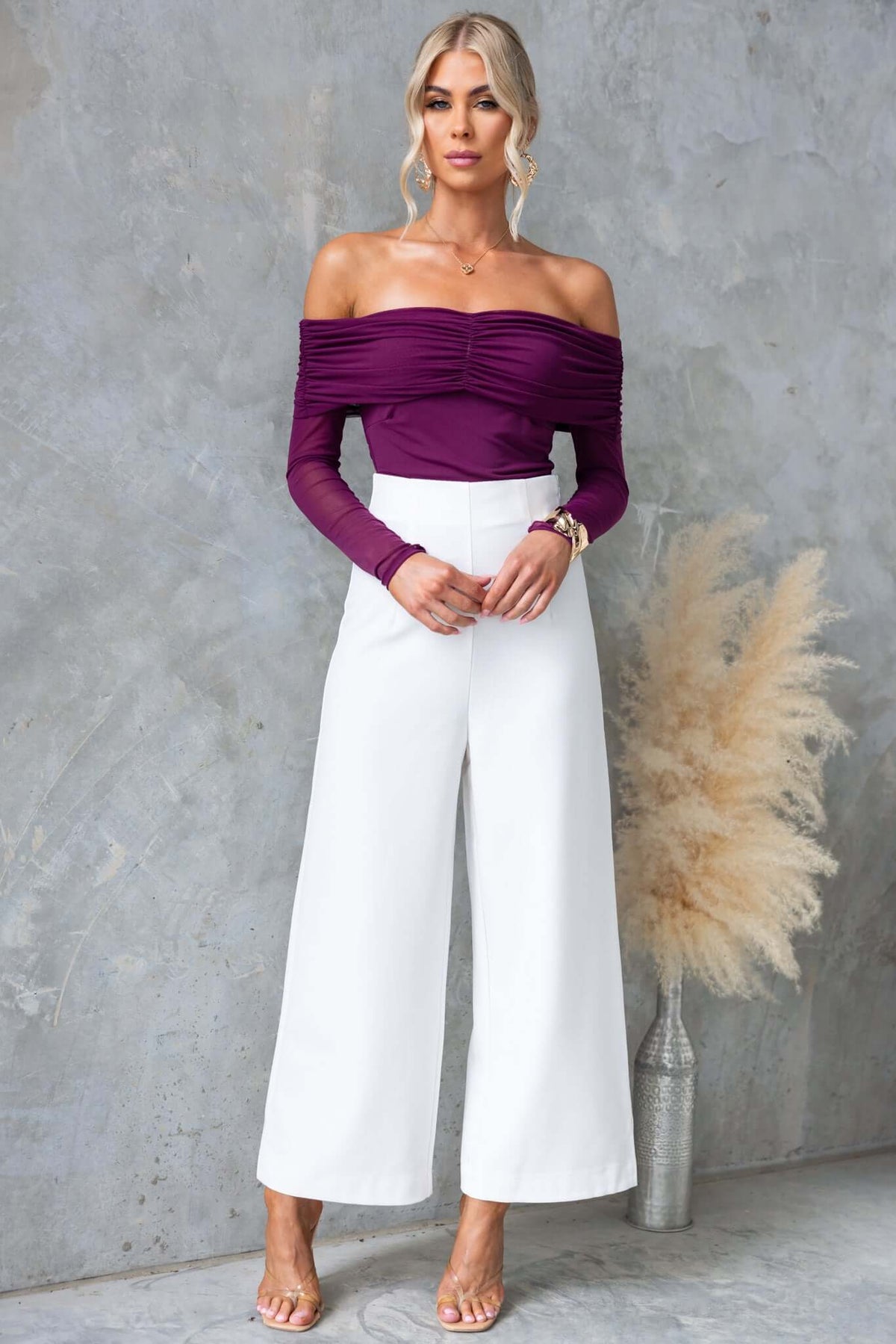 Model wearing Arcanna top with off-shoulder neckline and white wide-leg pants, showcasing stretchy purple fabric.