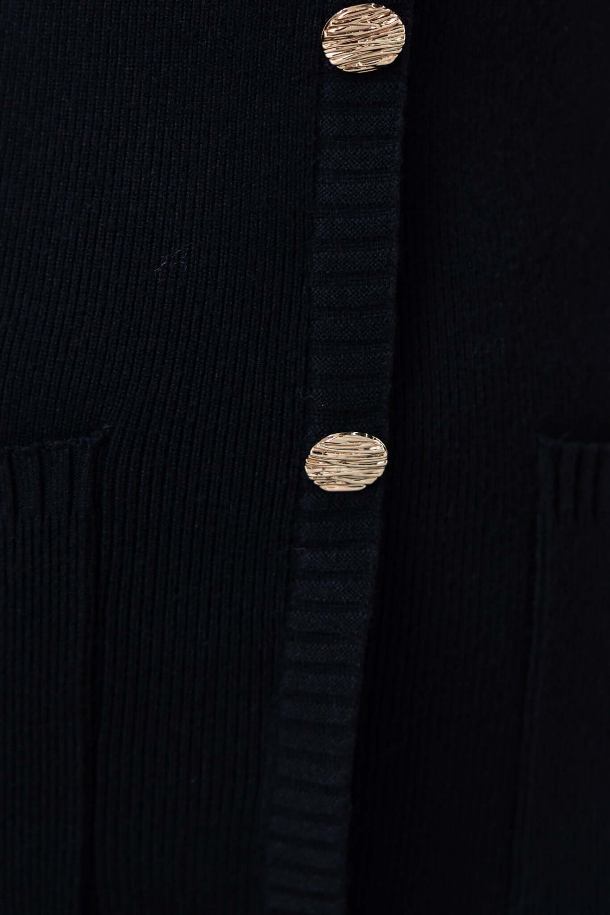 Close-up of a black knit cardigan featuring textured faux buttons and pockets, showcasing a stylish design.
