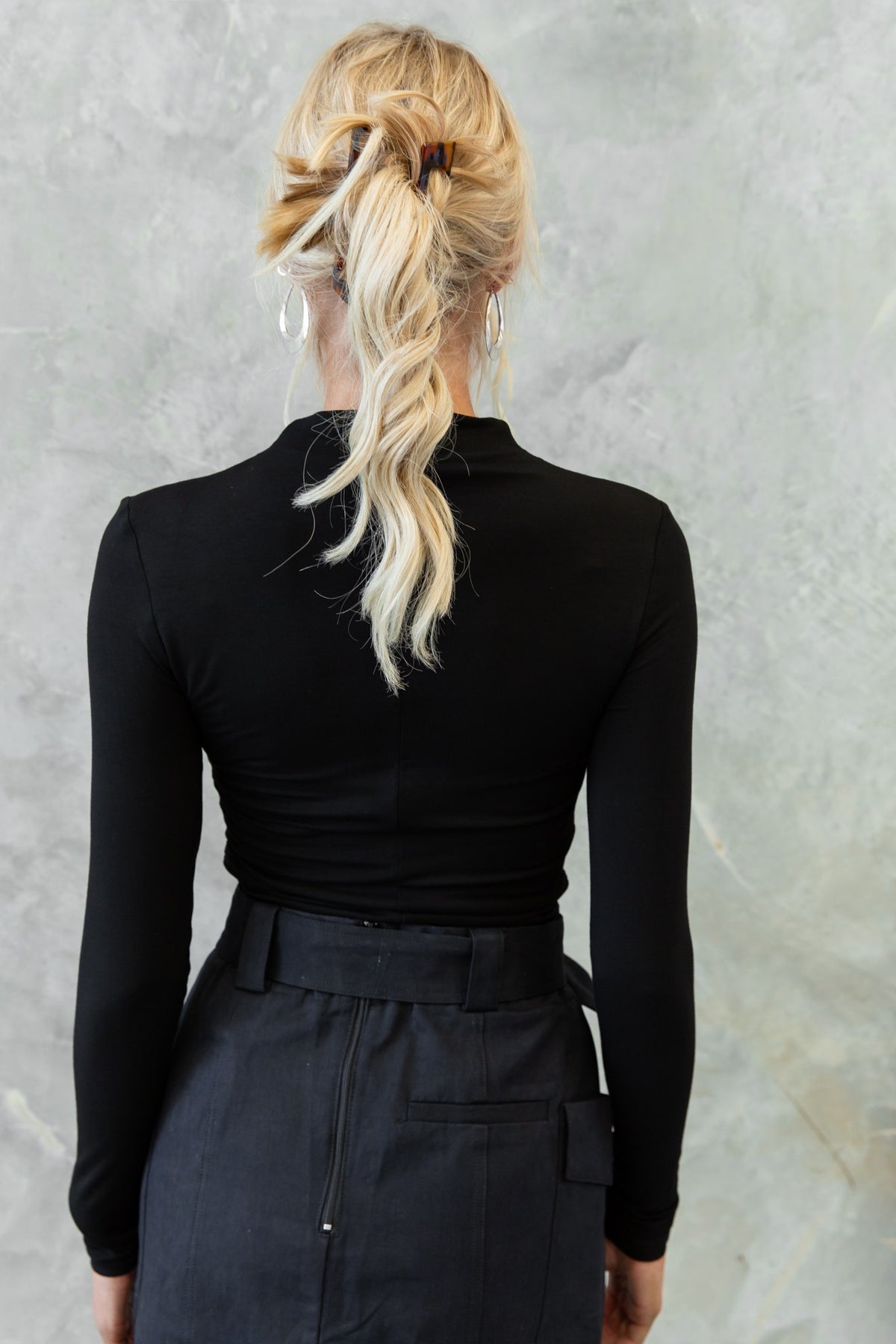 Back view of a woman wearing a black Rumba Top with long sleeves and a high neckline, styled with a chic ponytail.