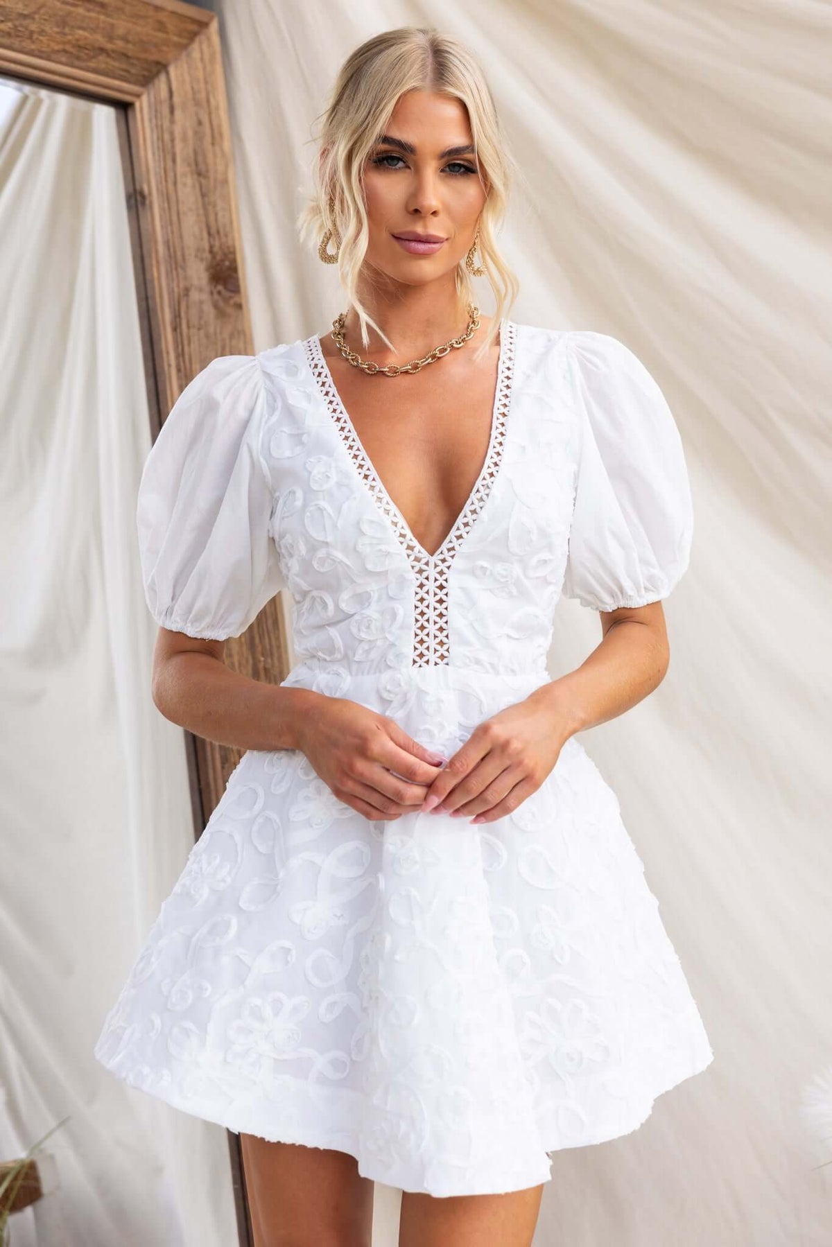 Casen Dress featuring a V-neckline and puff sleeves, styled by a model in white with intricate embroidery.