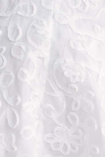 Close-up of delicate white embroidered pattern on fabric, showcasing intricate floral details for dress design.