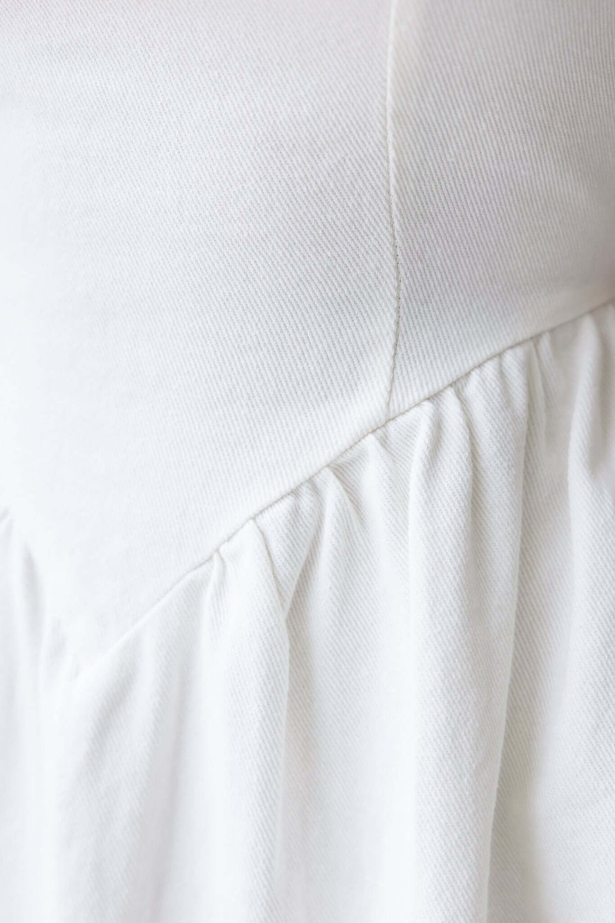 Close-up of the fabric texture and gathered waist detailing of a white dress, showcasing soft cotton material.
