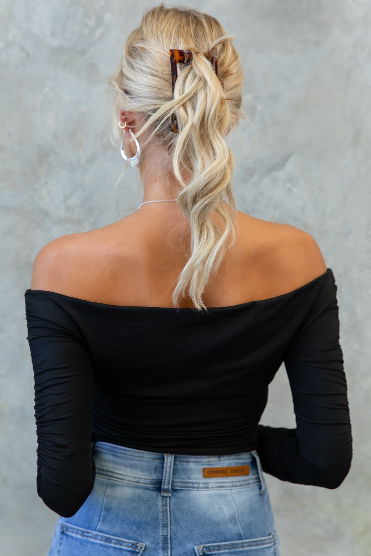 Model wearing Delvey off-shoulder bodysuit showcasing ruching detail and styled with high-waisted jeans.
