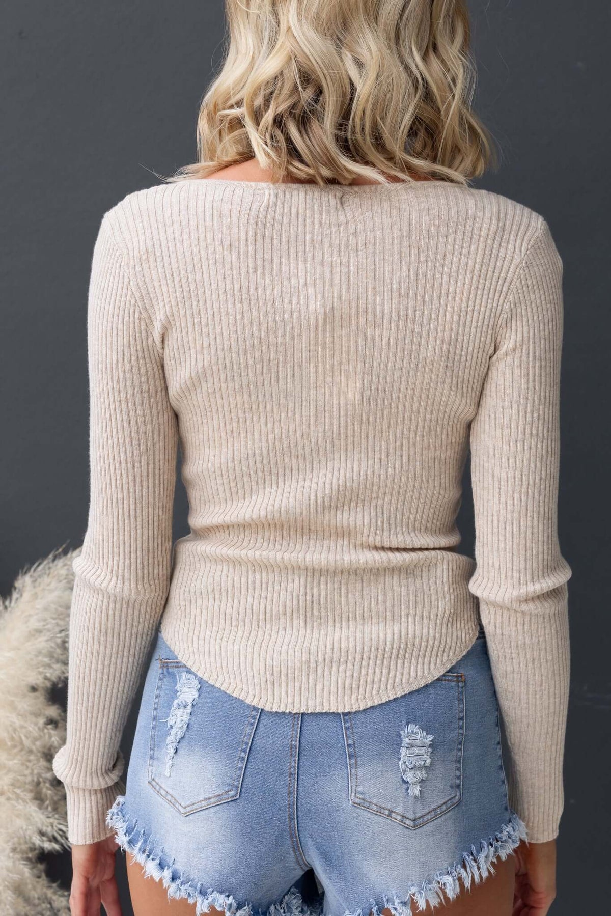 Back view of the Draw Me In Top featuring a round neckline and tapered hem, styled with distressed denim shorts.