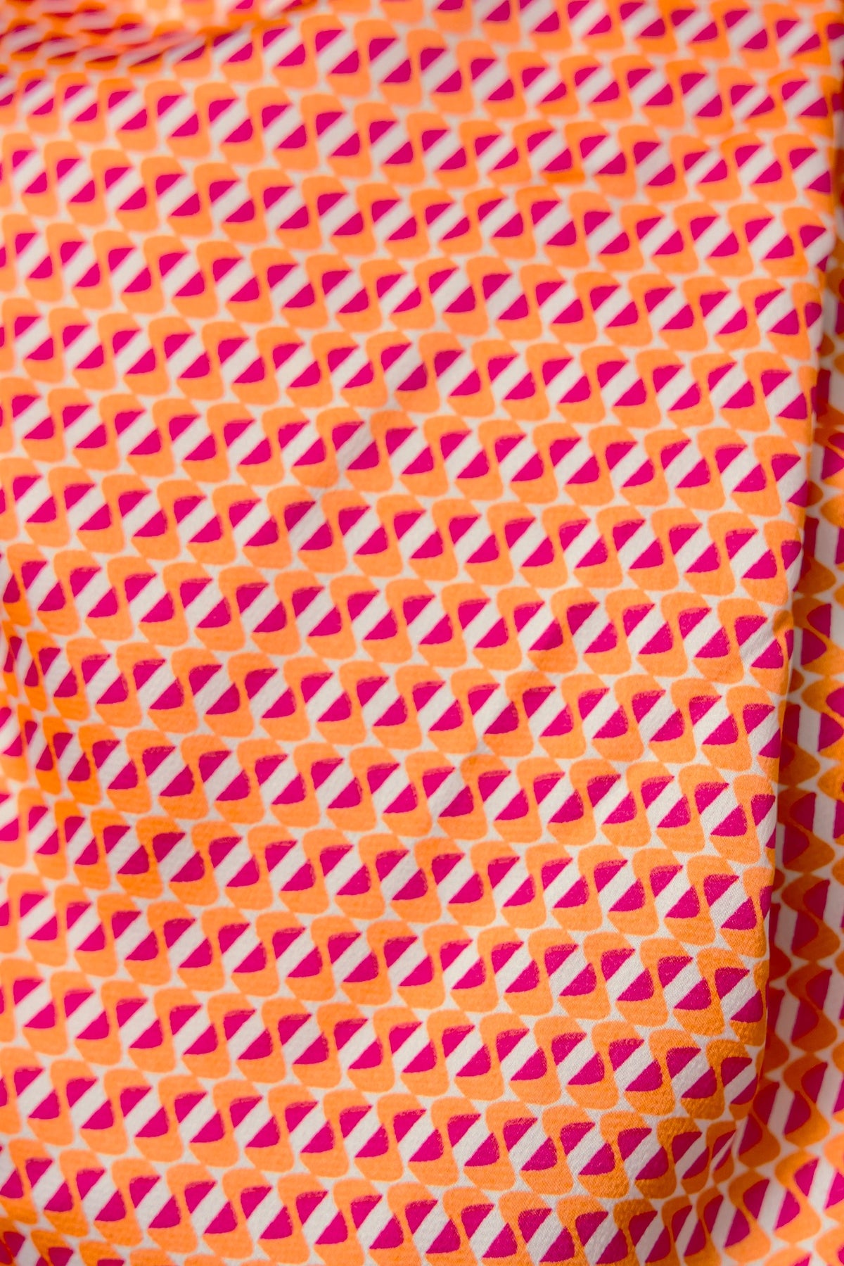 Colorful geometric pattern in shades of pink and orange on fabric, ideal for vibrant fashion designs.