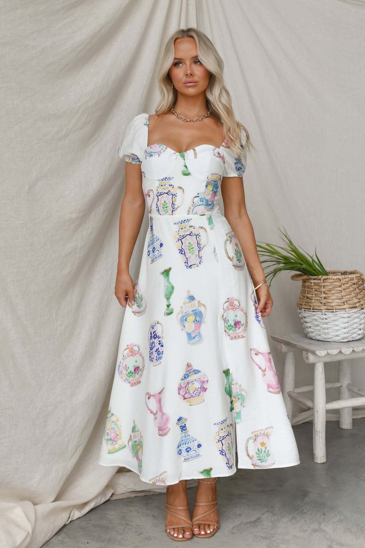 Woman wearing the Keyser Midi Dress with colorful vase patterns, featuring puff sleeves and a fitted bodice, in a stylish setting.