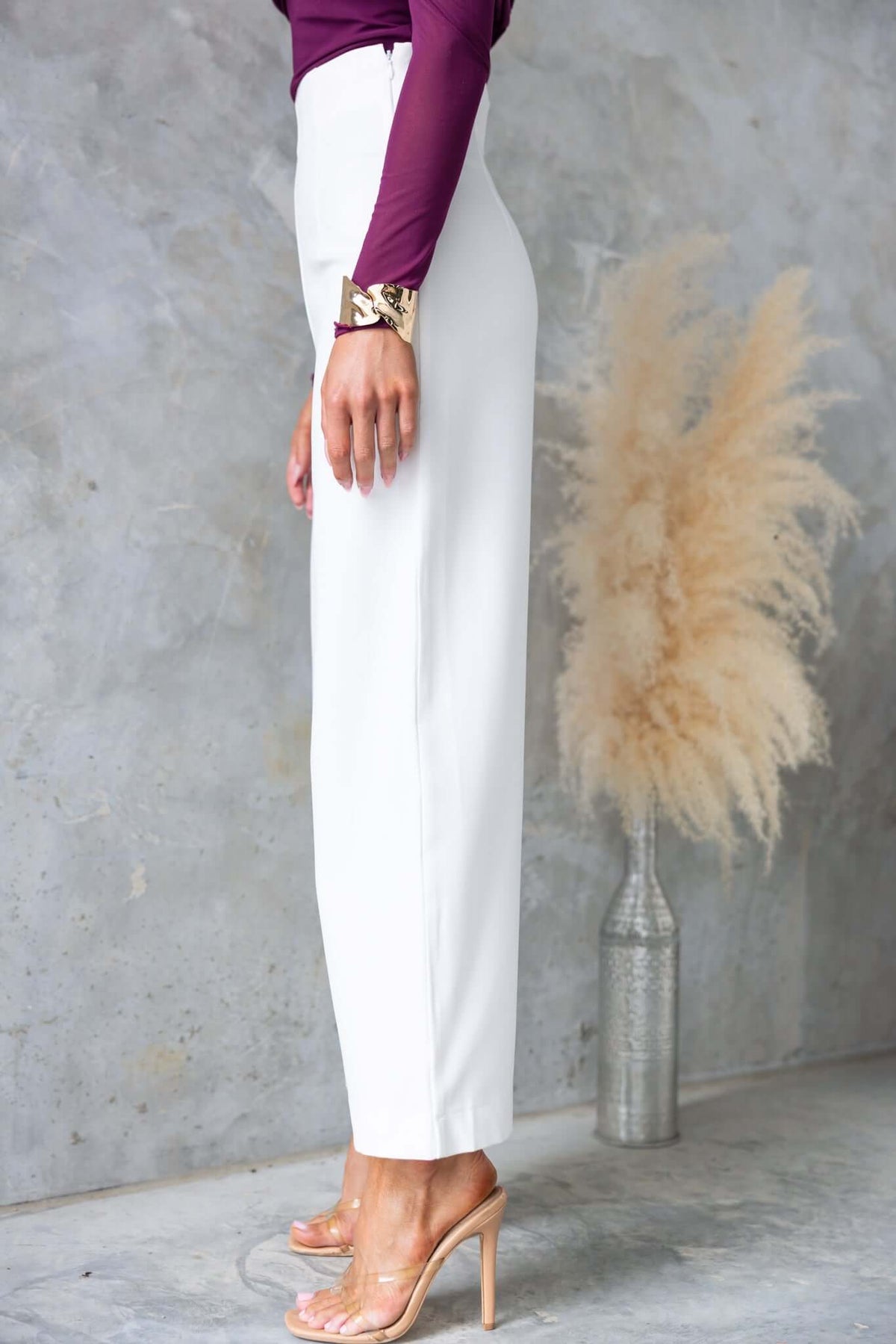 Side view of Edam Pants in white, featuring a mid-high waist and a side invisible zip, styled with a purple top.