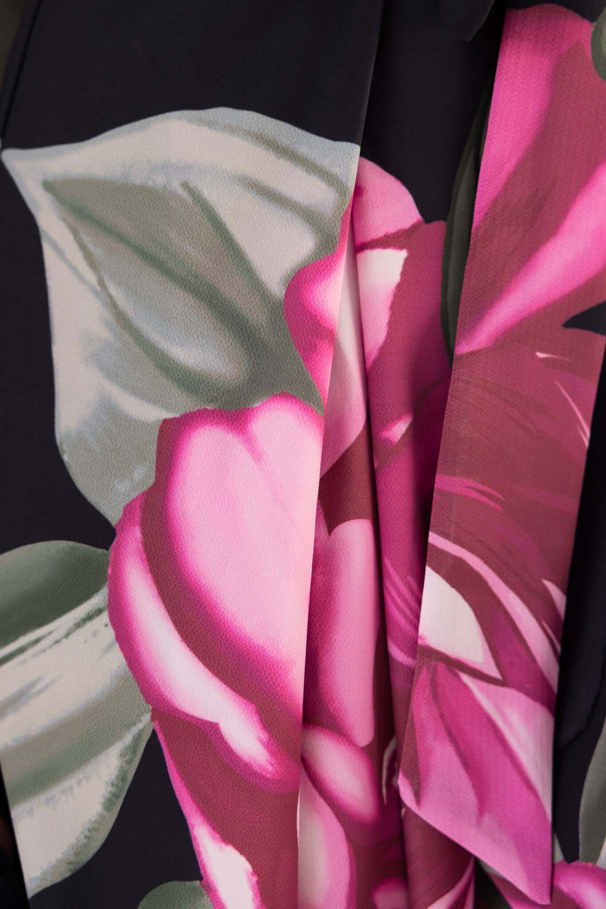 Close-up of floral print featuring pink flowers and green leaves on a dark background, showcasing fabric details.