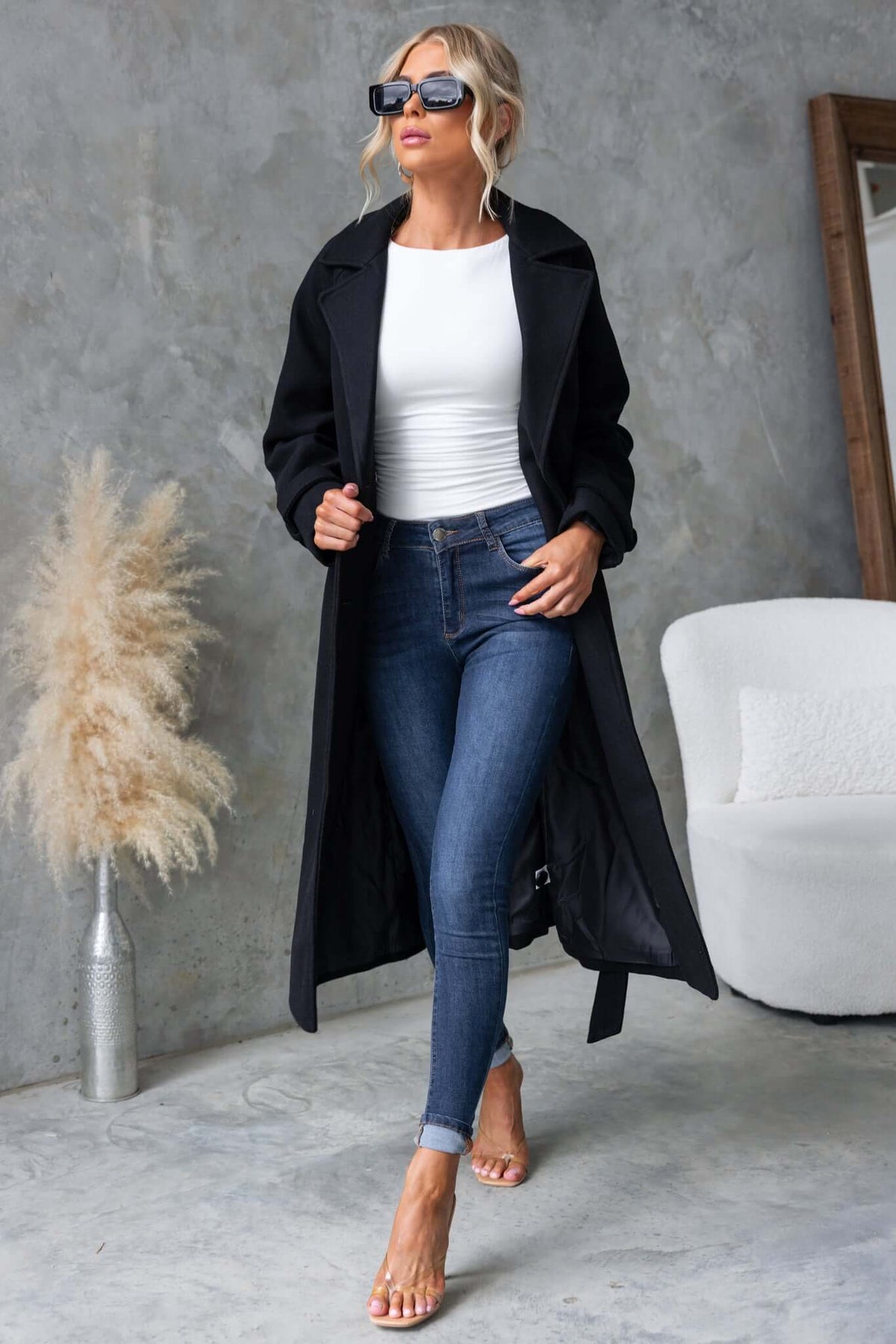 Model in a longline black Farina Coat, styled with jeans and a white top, showcasing the collar, lapel, and button-up front.