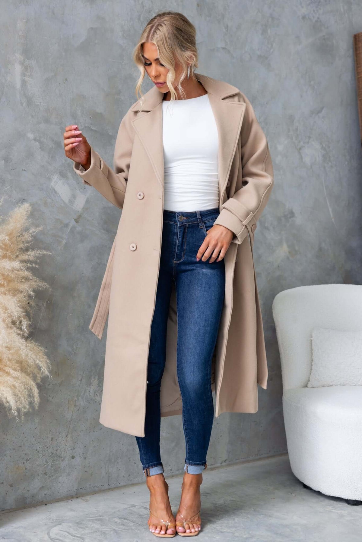 Farina coat in beige, longline fit with buttons, worn over a white top and blue jeans, styled with heels.