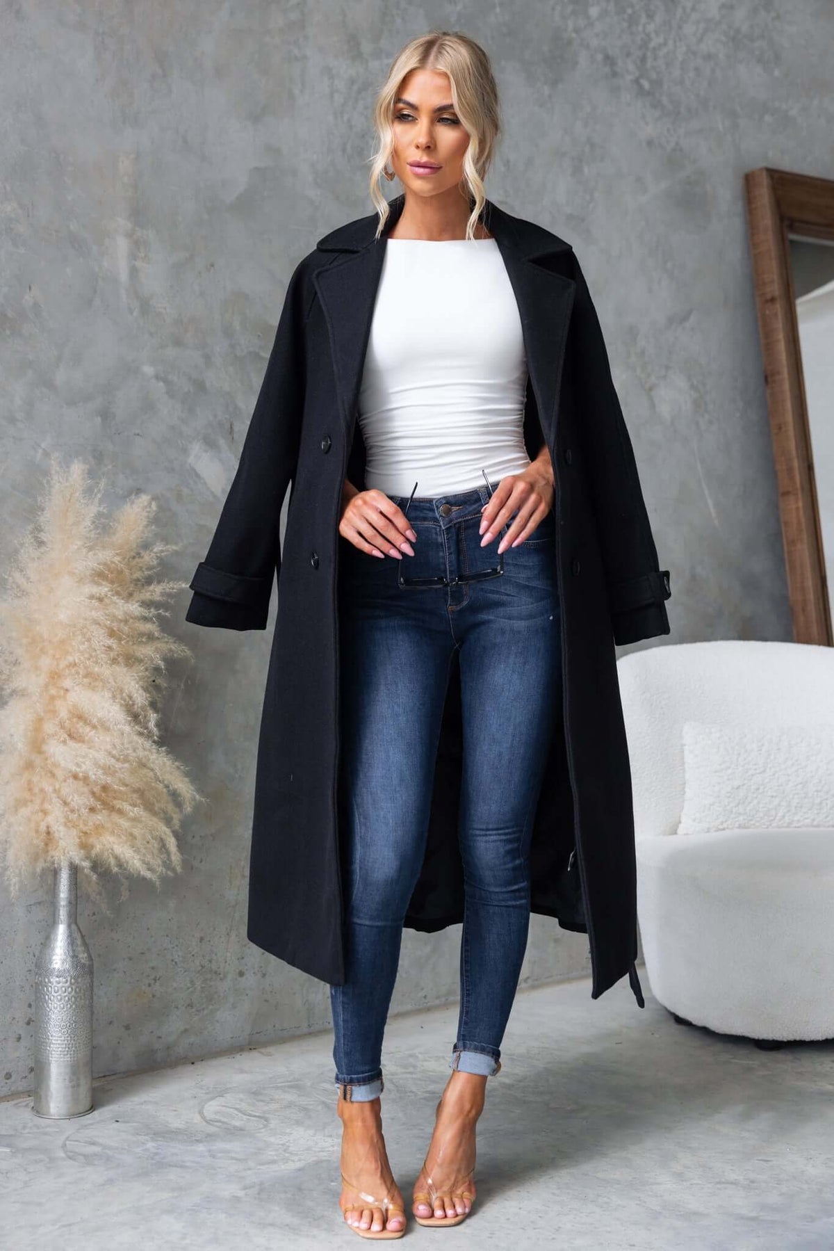 Farina Coat in black on model wearing jeans and a white top, showcasing longline fit and collar design.