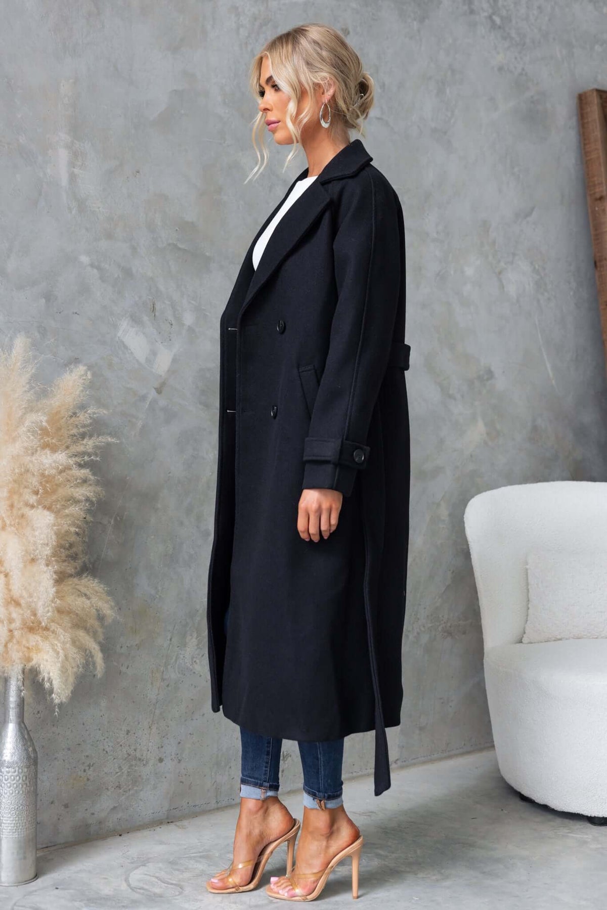 Model showcasing the Farina Coat, a longline black coat with a collar, button-up front, and removable tie.
