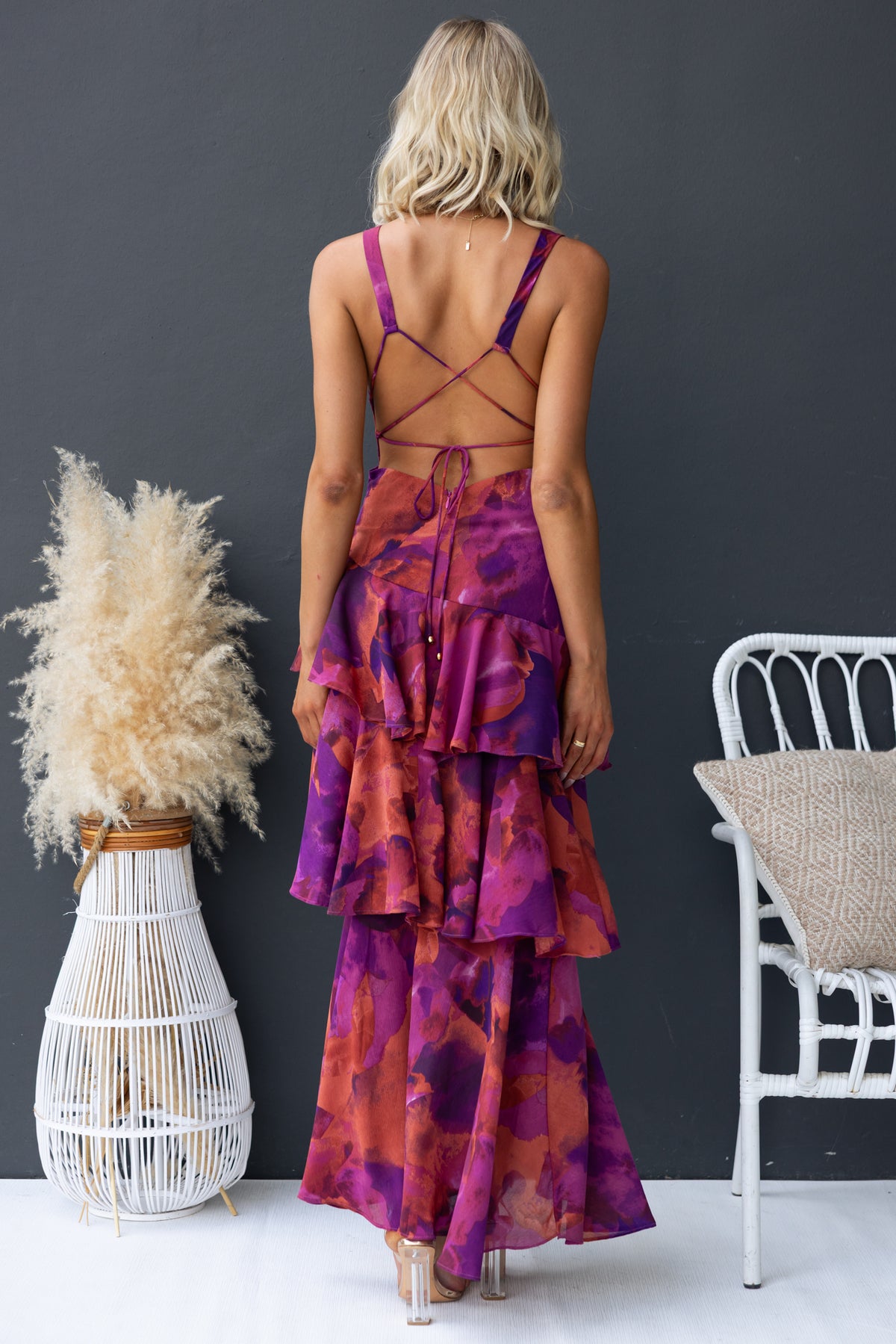 Back view of a floral print maxi dress with ruffle hem and tied straps, showcasing vibrant purple and orange colors.