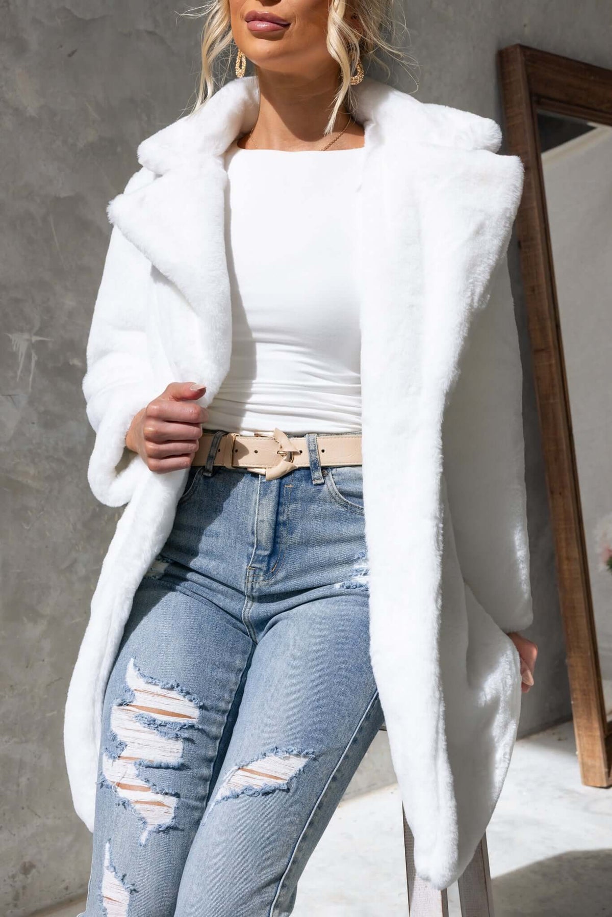 Stylish woman in a fluffy white frosted coat with a collar, paired with ripped jeans and a beige belt.
