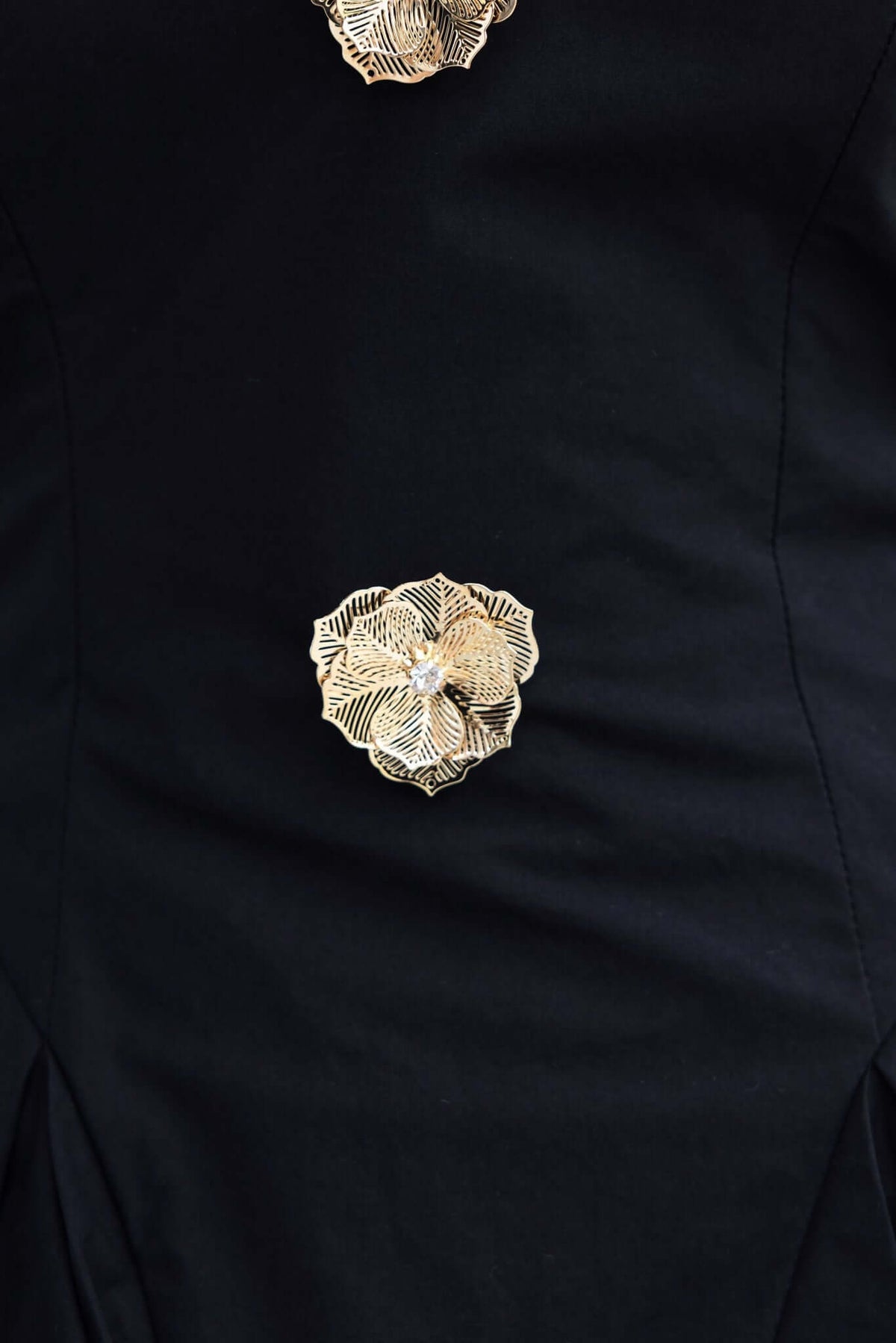 Close-up of the removable brooches on the Harbour Dress, featuring intricate gold floral designs on a black fabric.