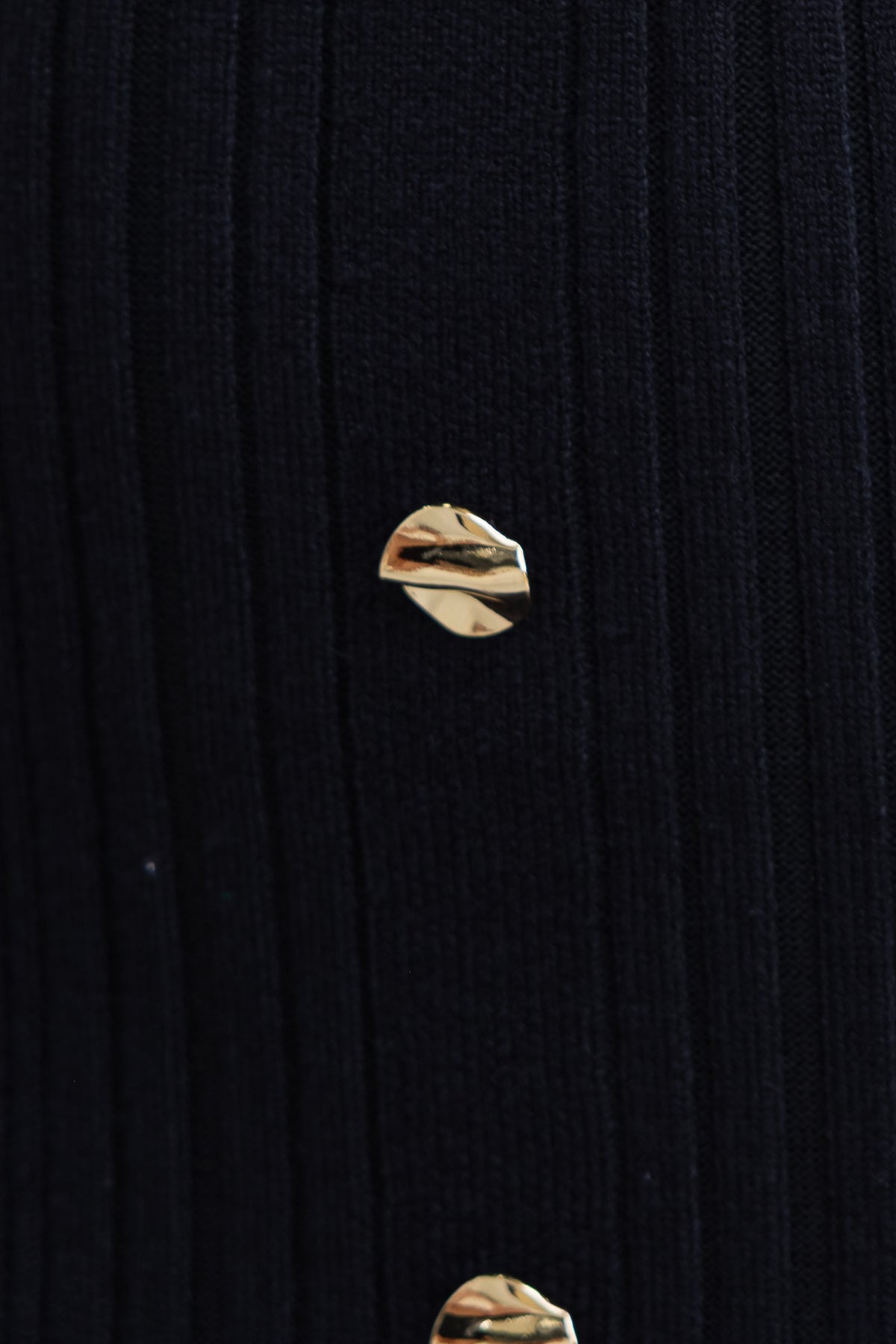 Close-up of faux buttons on a black knit dress, showcasing stylish details and texture.