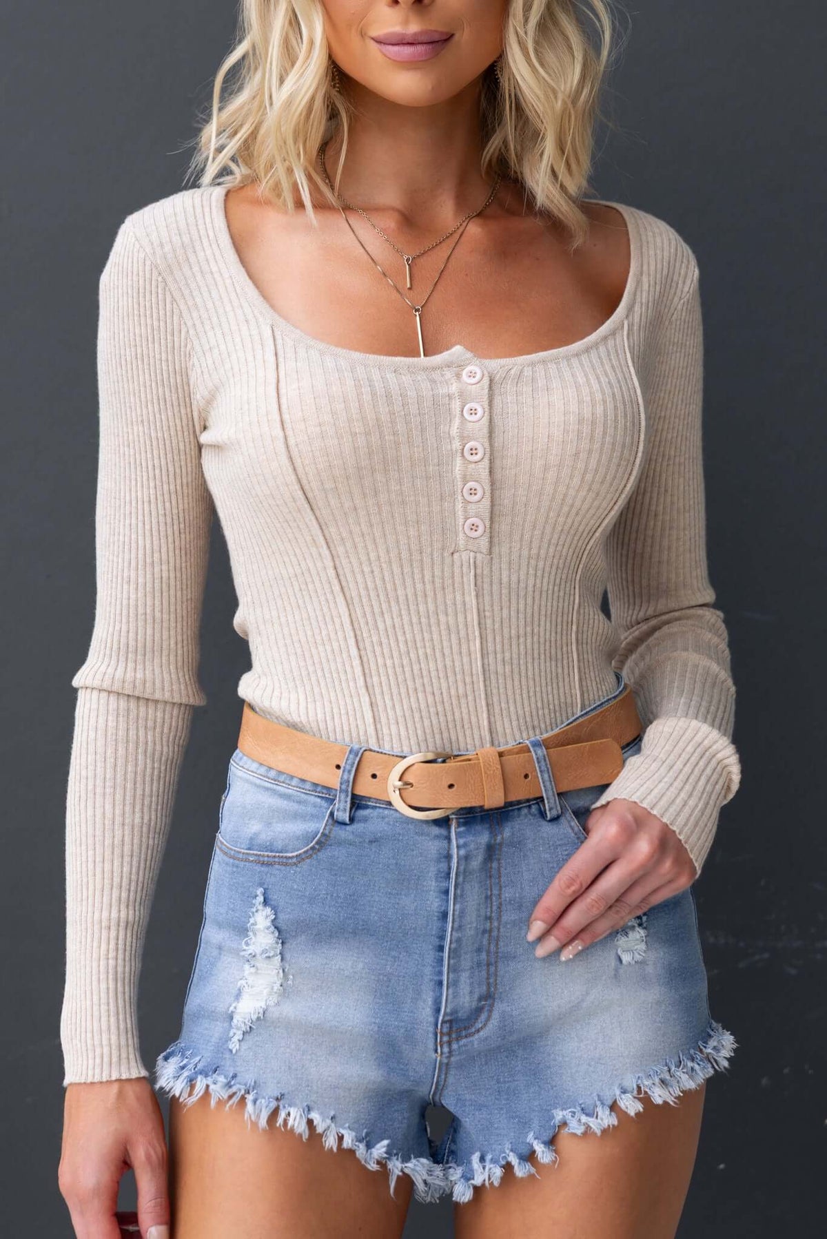 Model wearing Pecos Denim Shorts with high waist fit, distressed details, and raw hem, paired with a beige ribbed top.