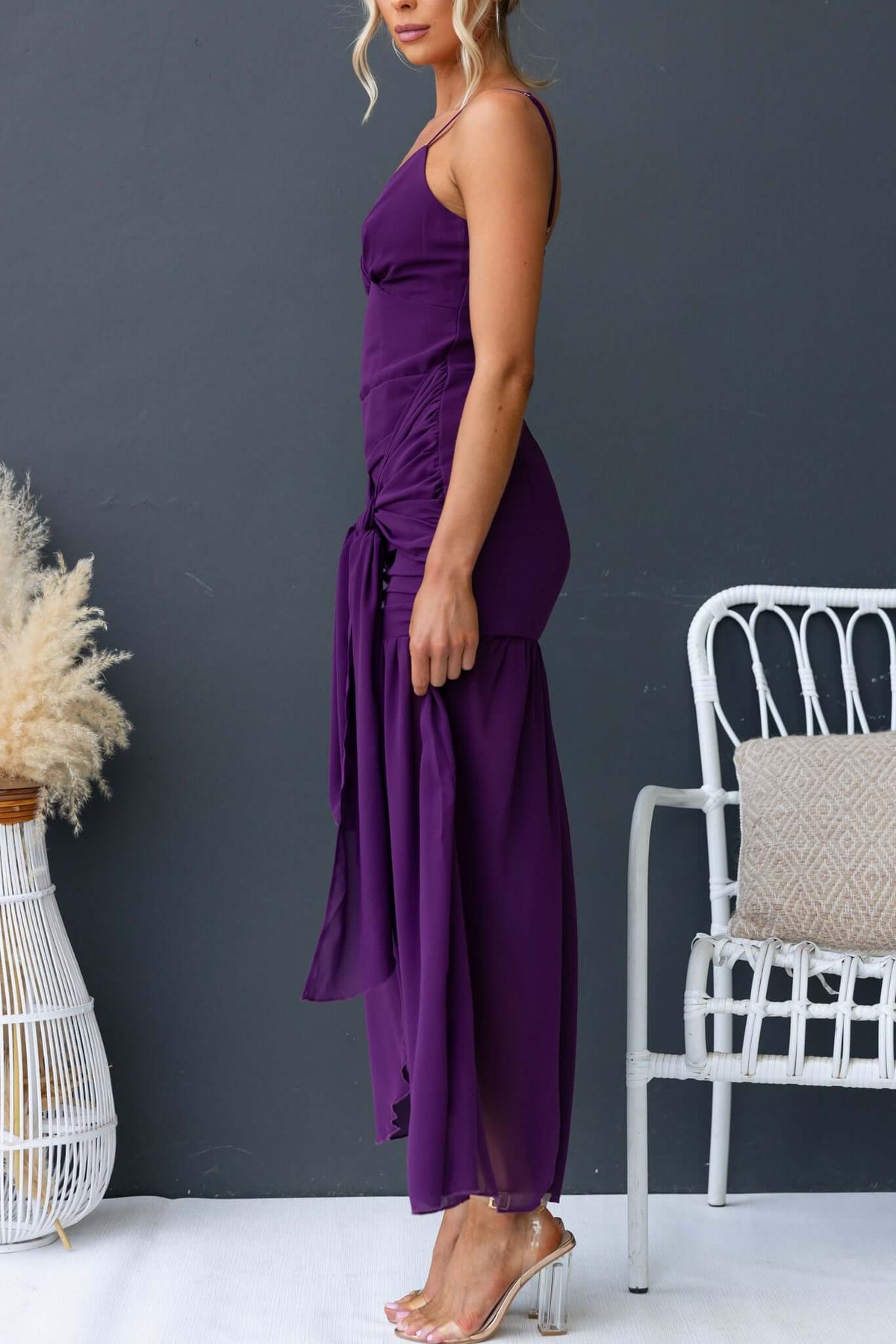 Woman wearing an iconic purple maxi dress with adjustable straps and a front split, styled in a modern setting.
