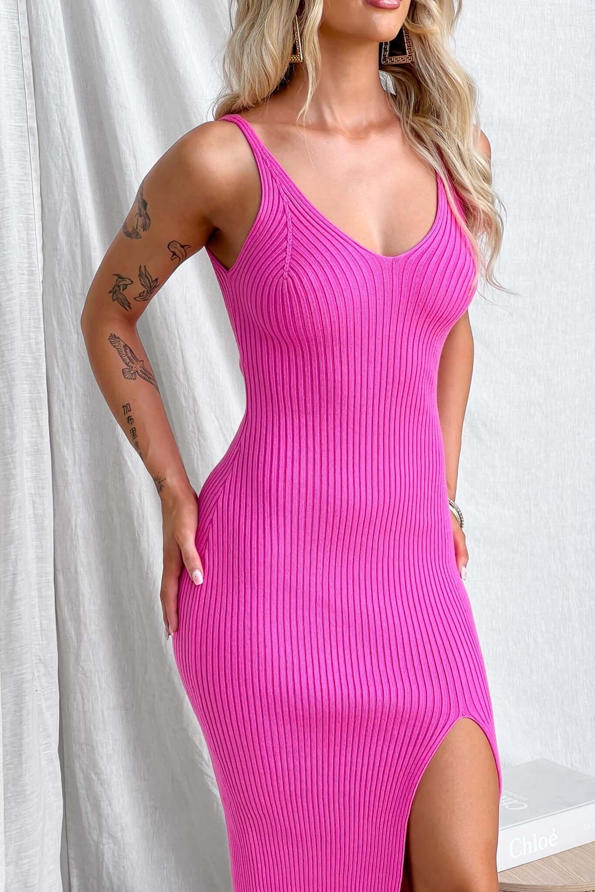 Pink ribbed midi dress with V-neckline and front split, featuring a form-fitting silhouette and comfortable stretch.