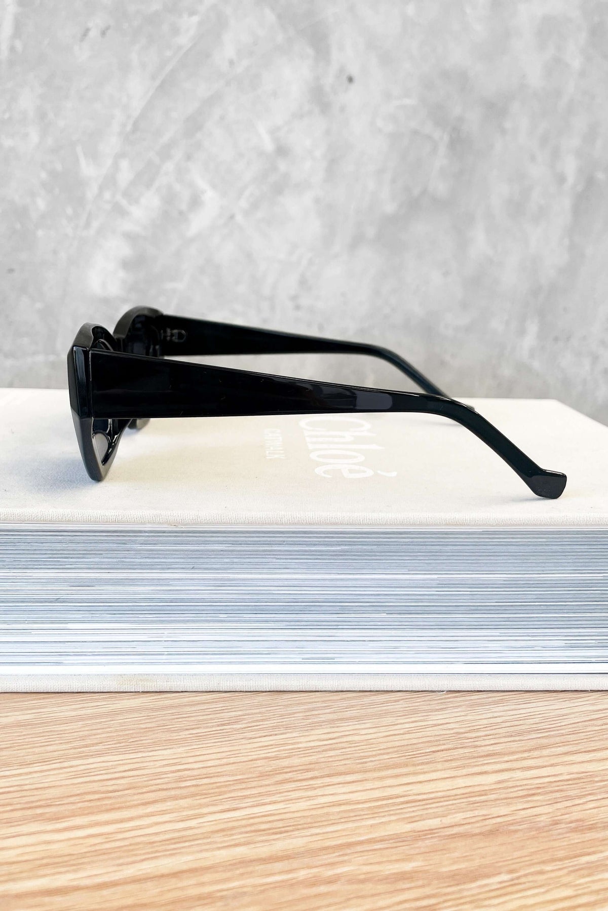 Side view of stylish black sunglasses resting on a stack of books, showcasing their sleek design and modern look.