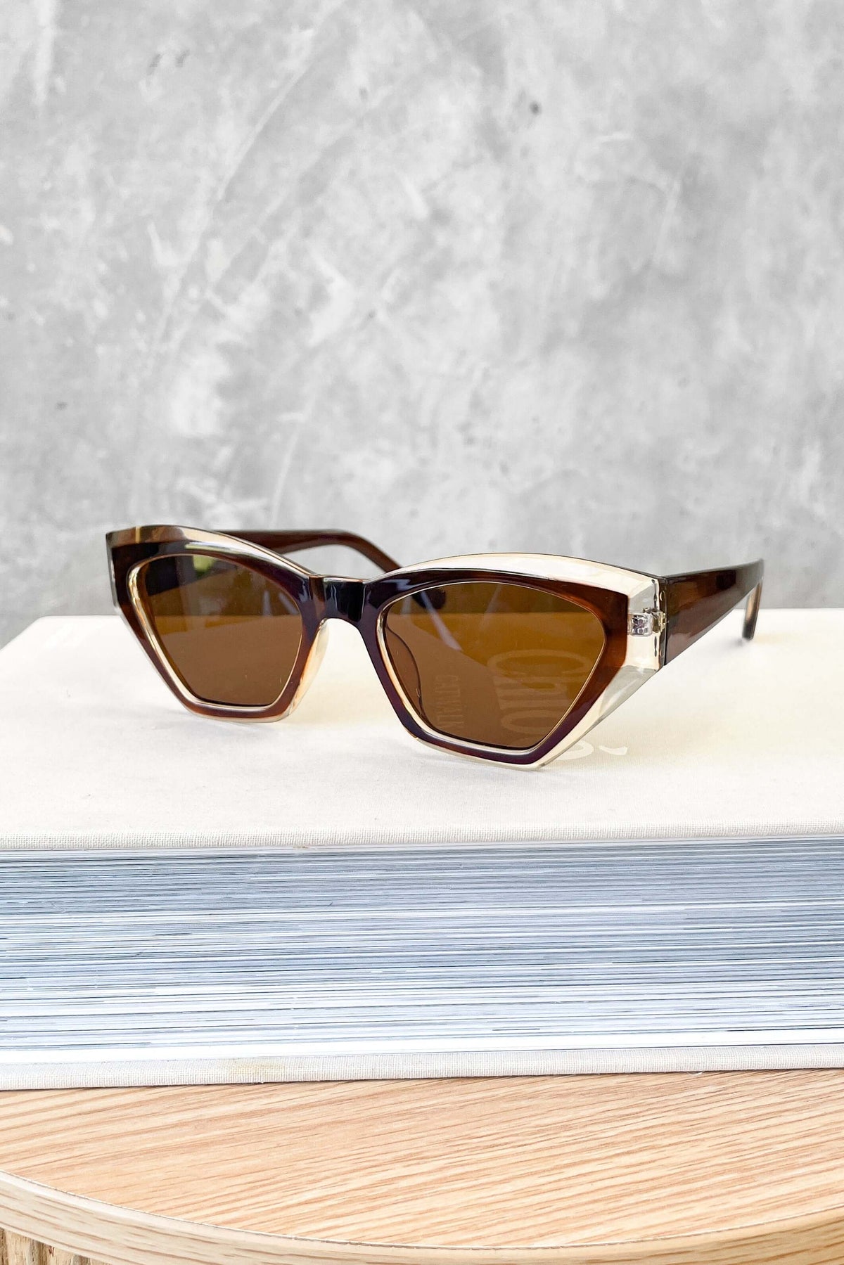 Stylish brown sunglasses on a light surface, featuring a chic cat-eye design and tinted lenses.