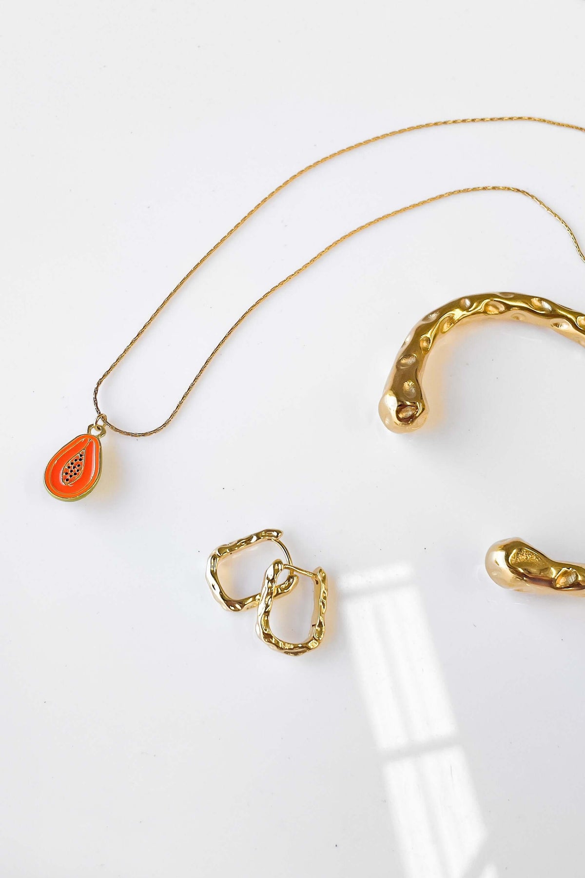 Gold Laila earrings and a necklace with an orange pendant on a white background, showcasing elegant jewelry design.