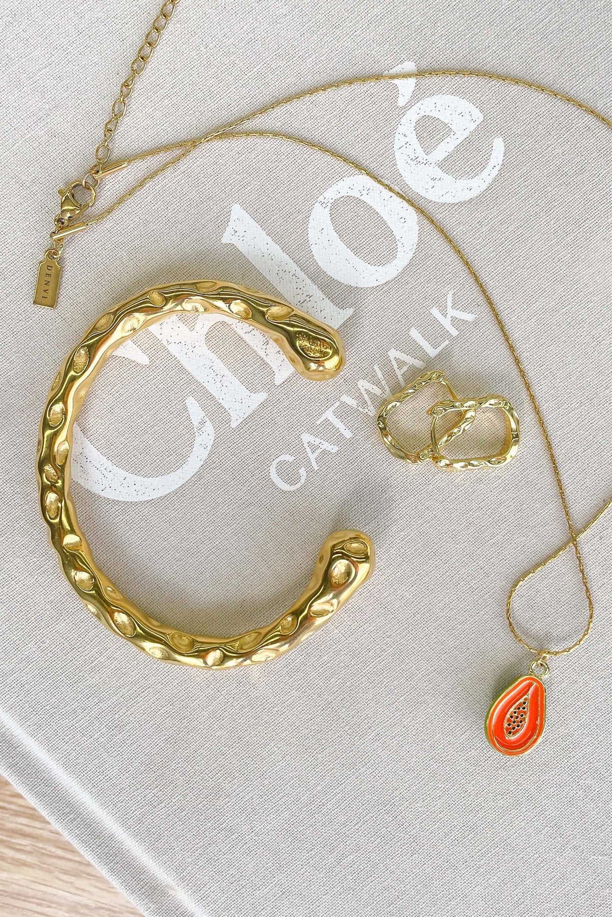 Stylish textured gold Ever After bracelet alongside other jewelry on a chic fashion book.