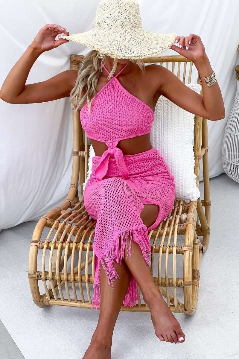 Model wearing a pink crochet midi dress with cut out sides and a tie at the neck, styled with a wide-brim hat.