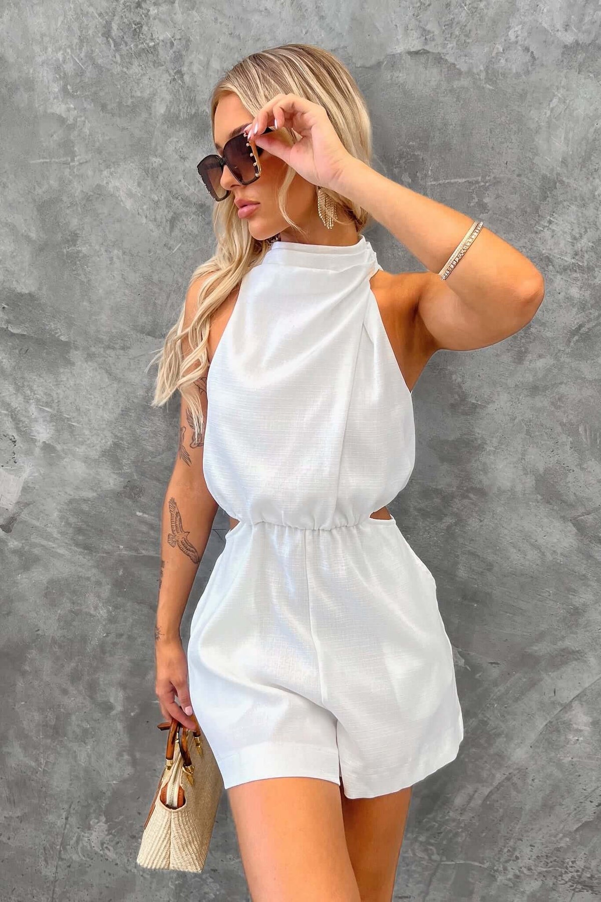 Model wearing a white timeless playsuit with high neckline, cut-out at waist, and stylish accessories.