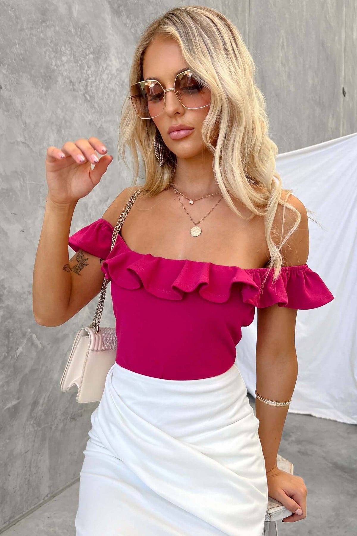 Model wearing Bellar Bodysuit in fuchsia with frill detail and off-shoulder design, paired with a white skirt.