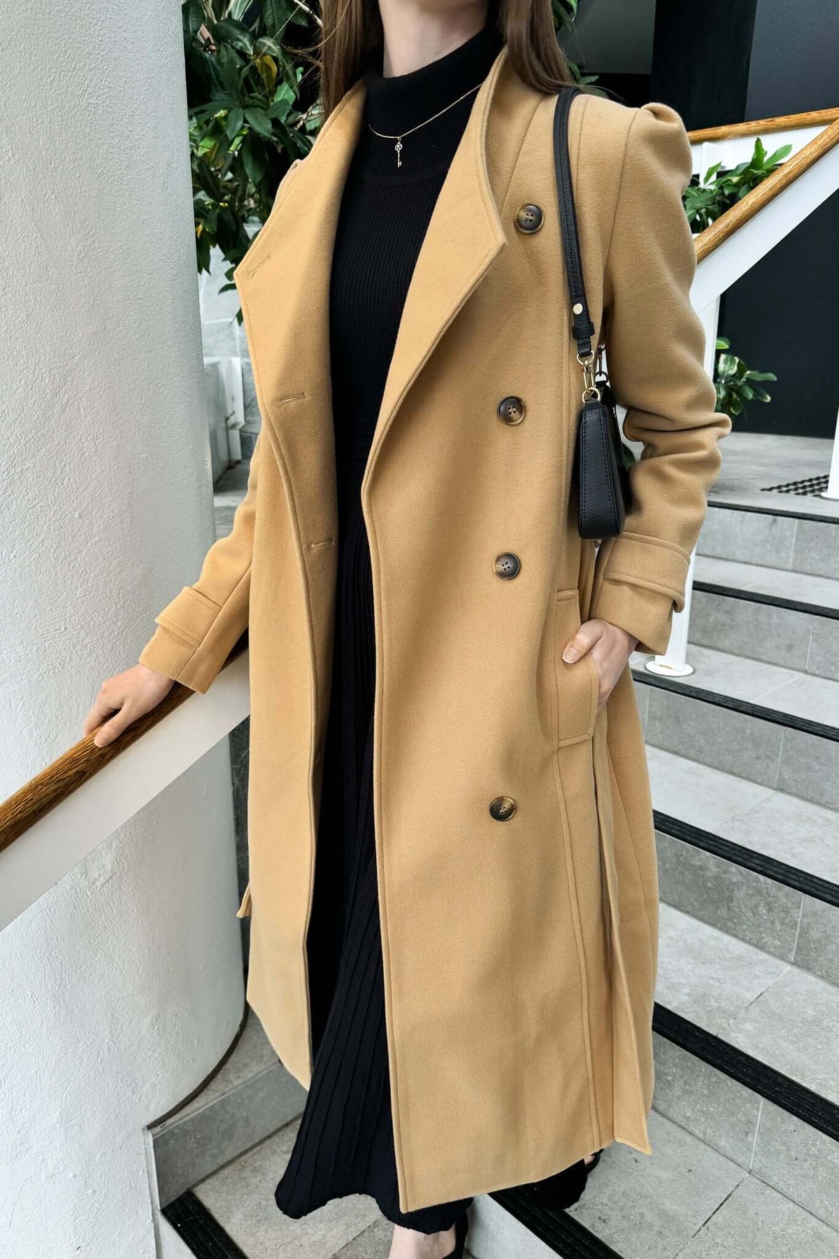 Model wearing a stylish longline Ortona coat with a collar, button-up front, and removable fabric tie.