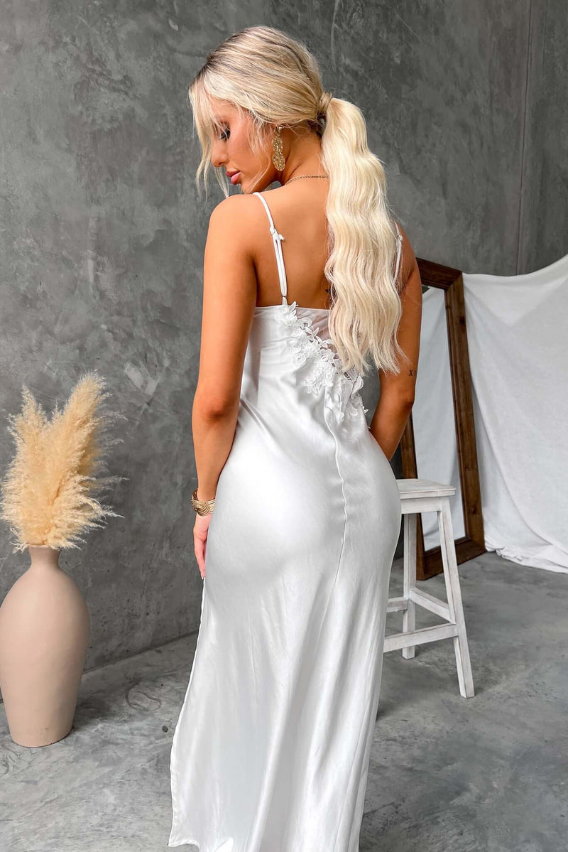 Back view of a woman in a white maxi dress with adjustable straps and a mesh panel, styled in a modern interior.